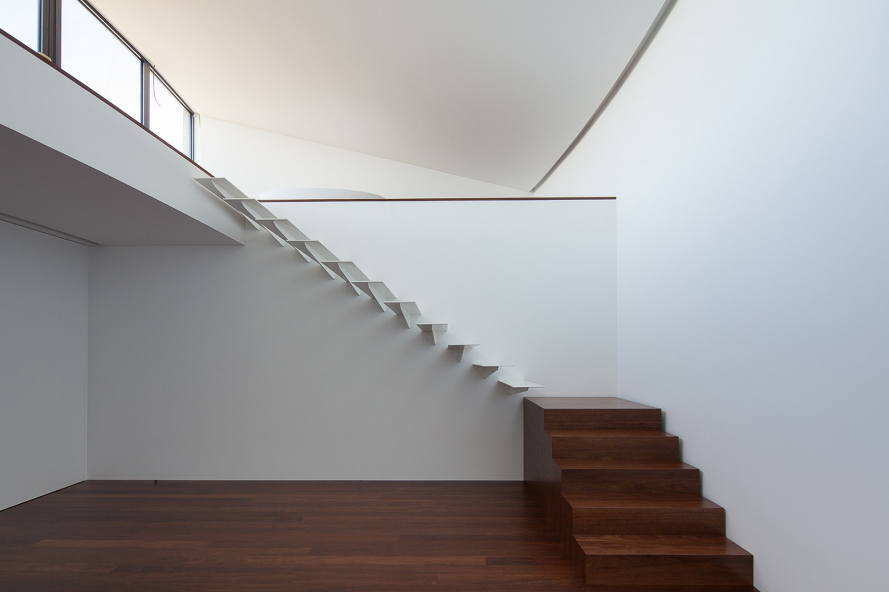 White cantilevered stair beside a timber block stair, beneath a curved ceiling lit by a clerestory window