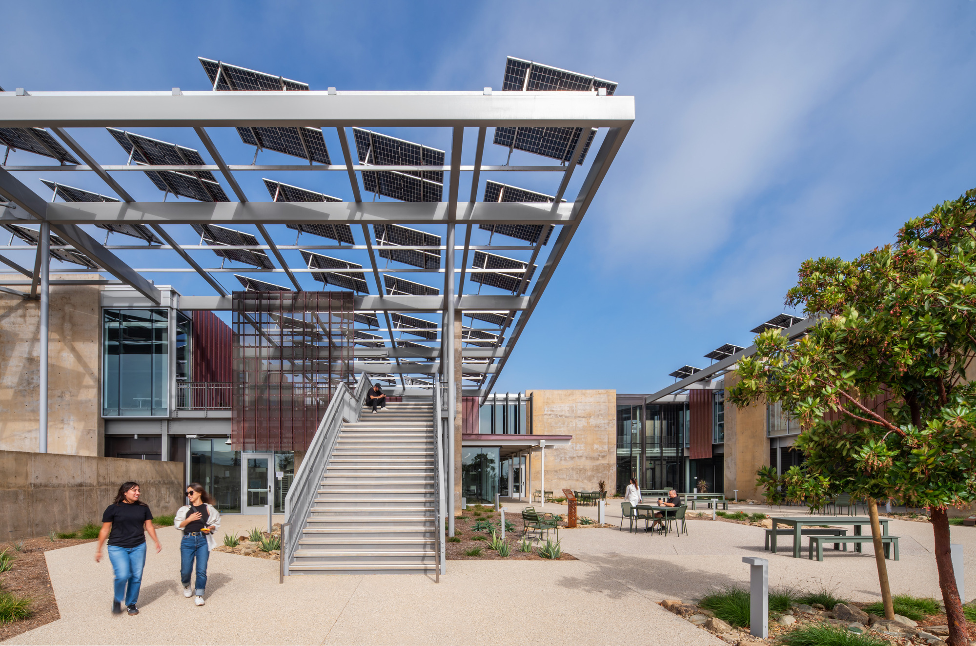 White steel staircase ascending through solar panel canopy as two visitors walk past planted beds