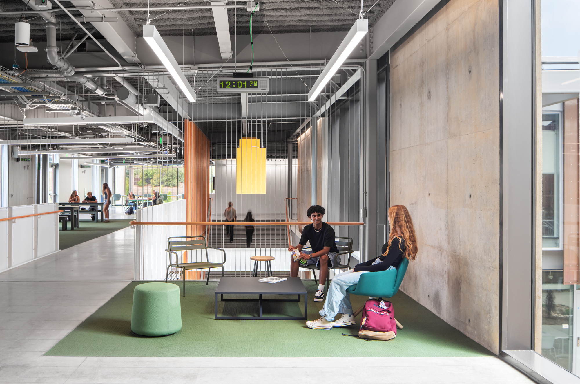Seating nook with concrete wall, yellow pendant light, and wire mesh partitions dividing workspace zones