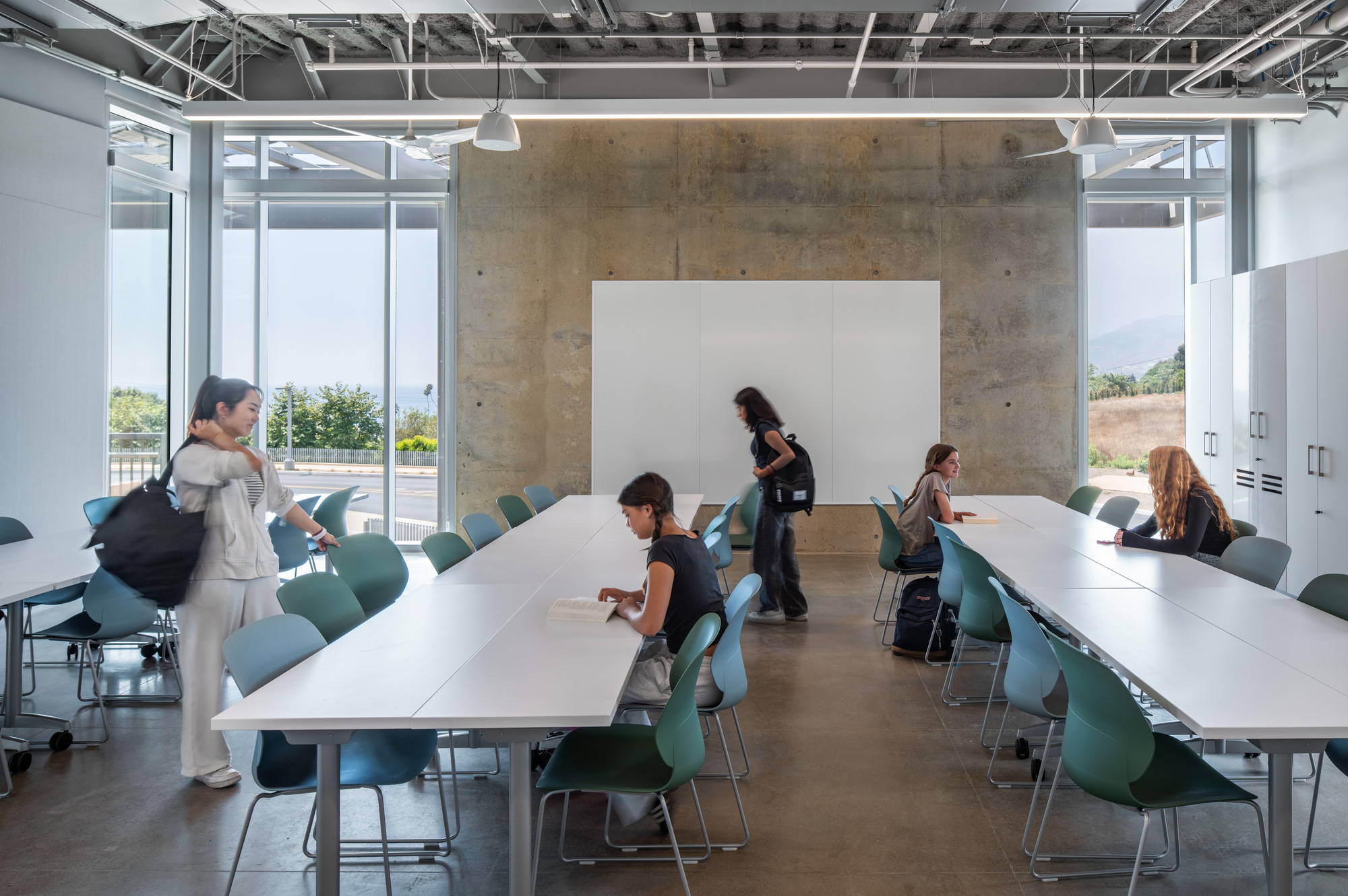 Meeting room with white tables, green chairs, concrete wall, and whiteboard mounted against exposed services