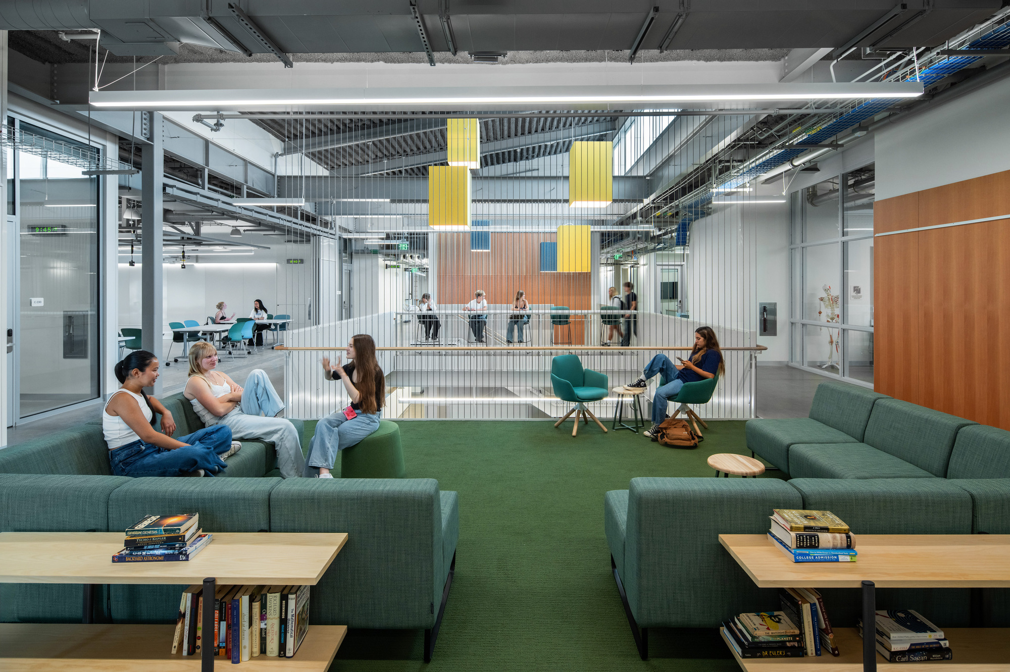 Common area with wire mesh dividers, hanging acoustic panels, and groups seated on green upholstered furniture