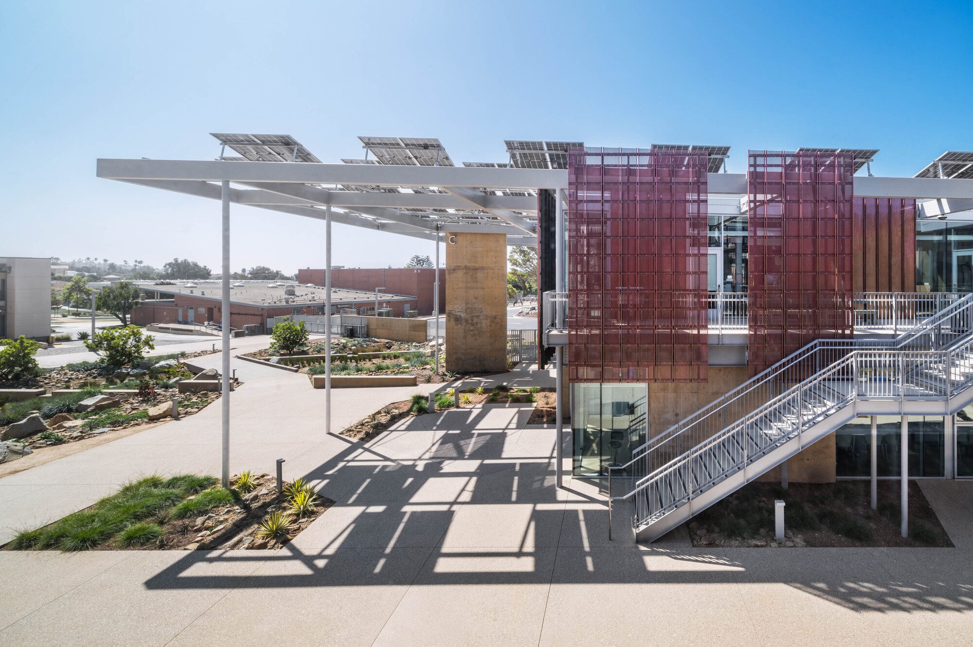 Exterior stair with metal railings ascending to upper level beneath a cantilevered solar panel canopy
