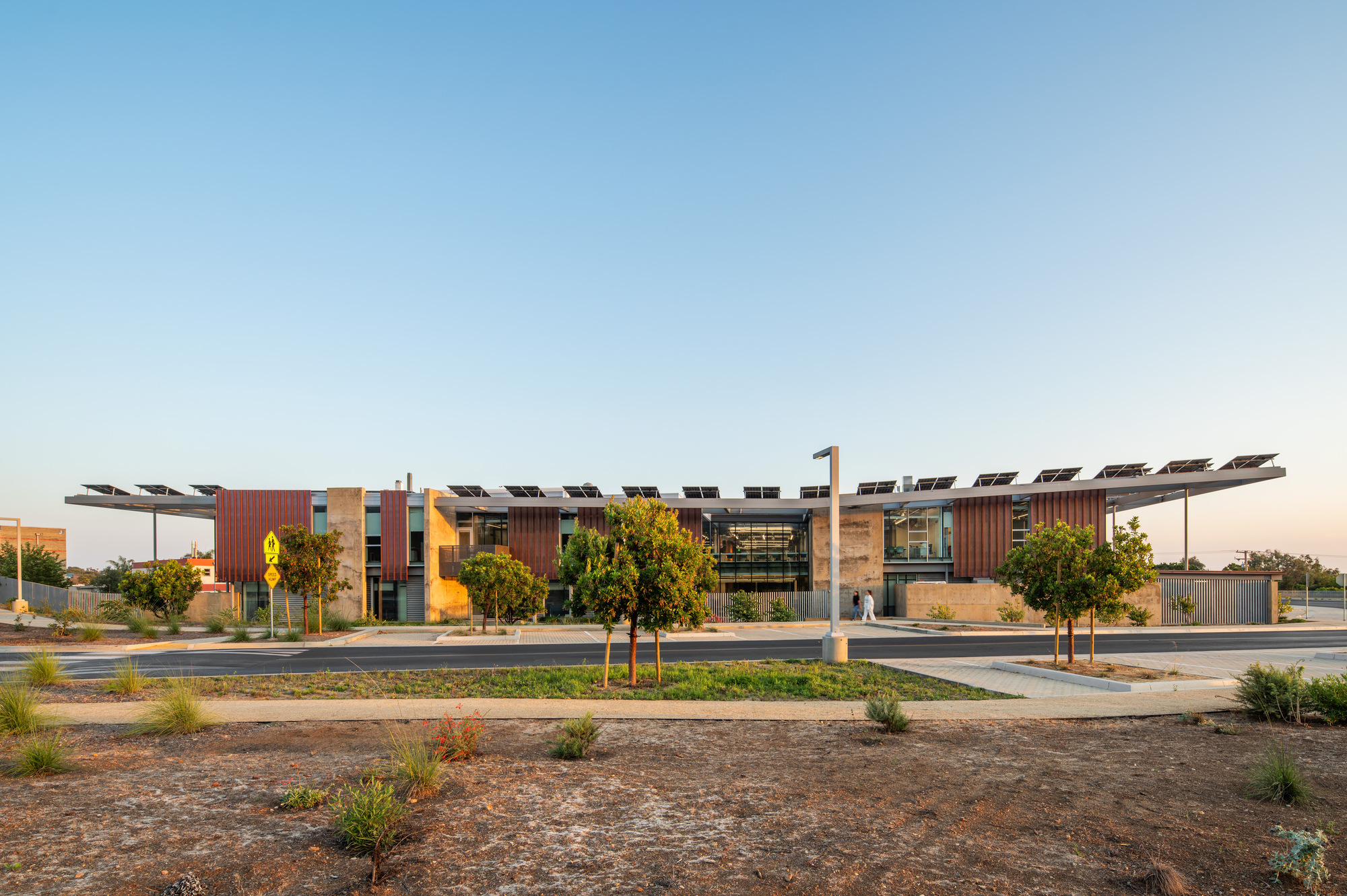 Street view of the vertical timber-clad volumes with cantilevered solar panel canopy at dusk