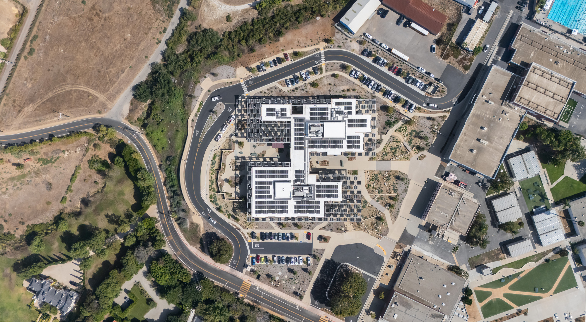 Aerial view of the curved campus building with white rooftop solar arrays and surrounding parking