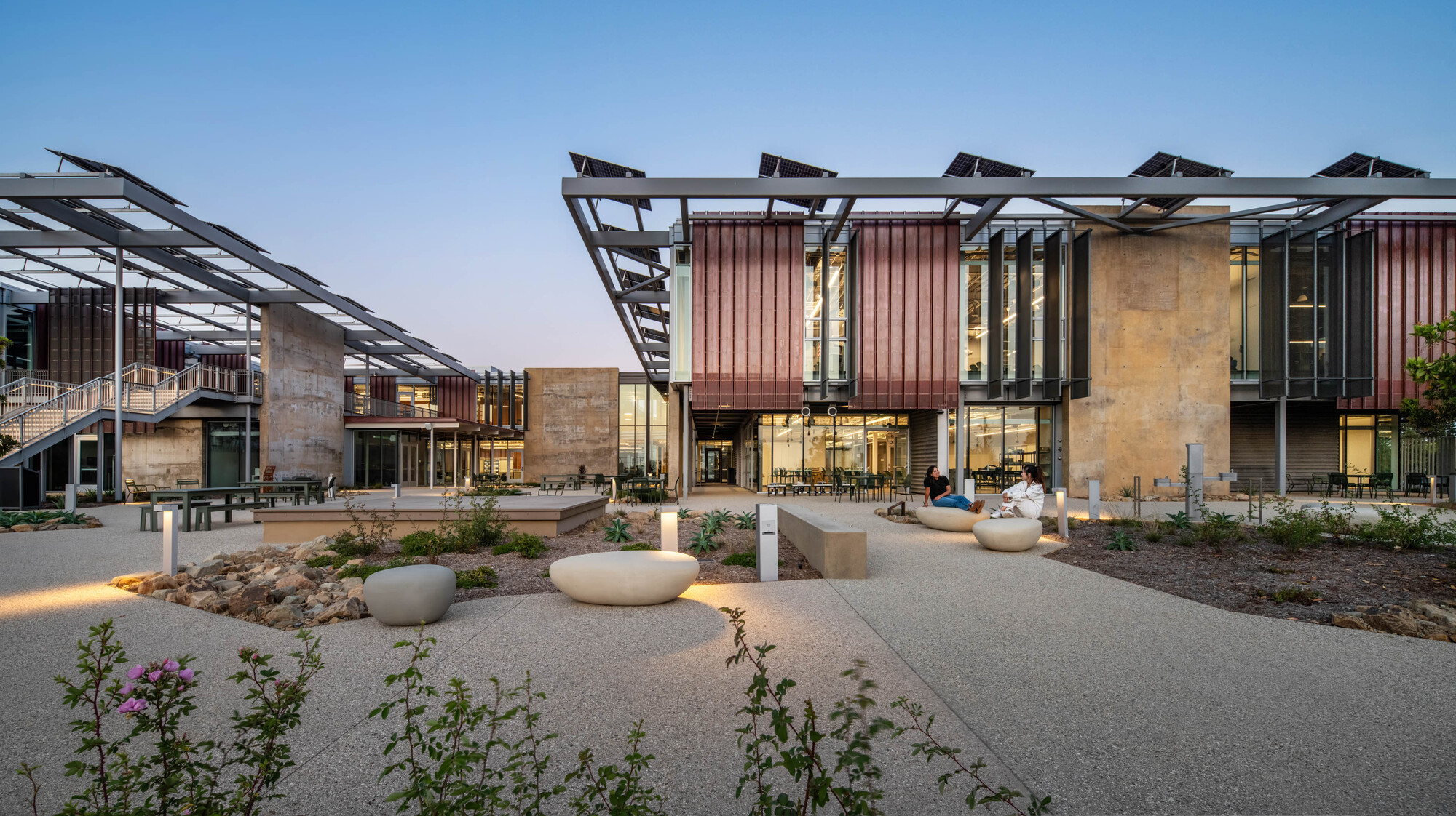 Central courtyard with gravel paths, planted beds, and timber-clad facades at twilight