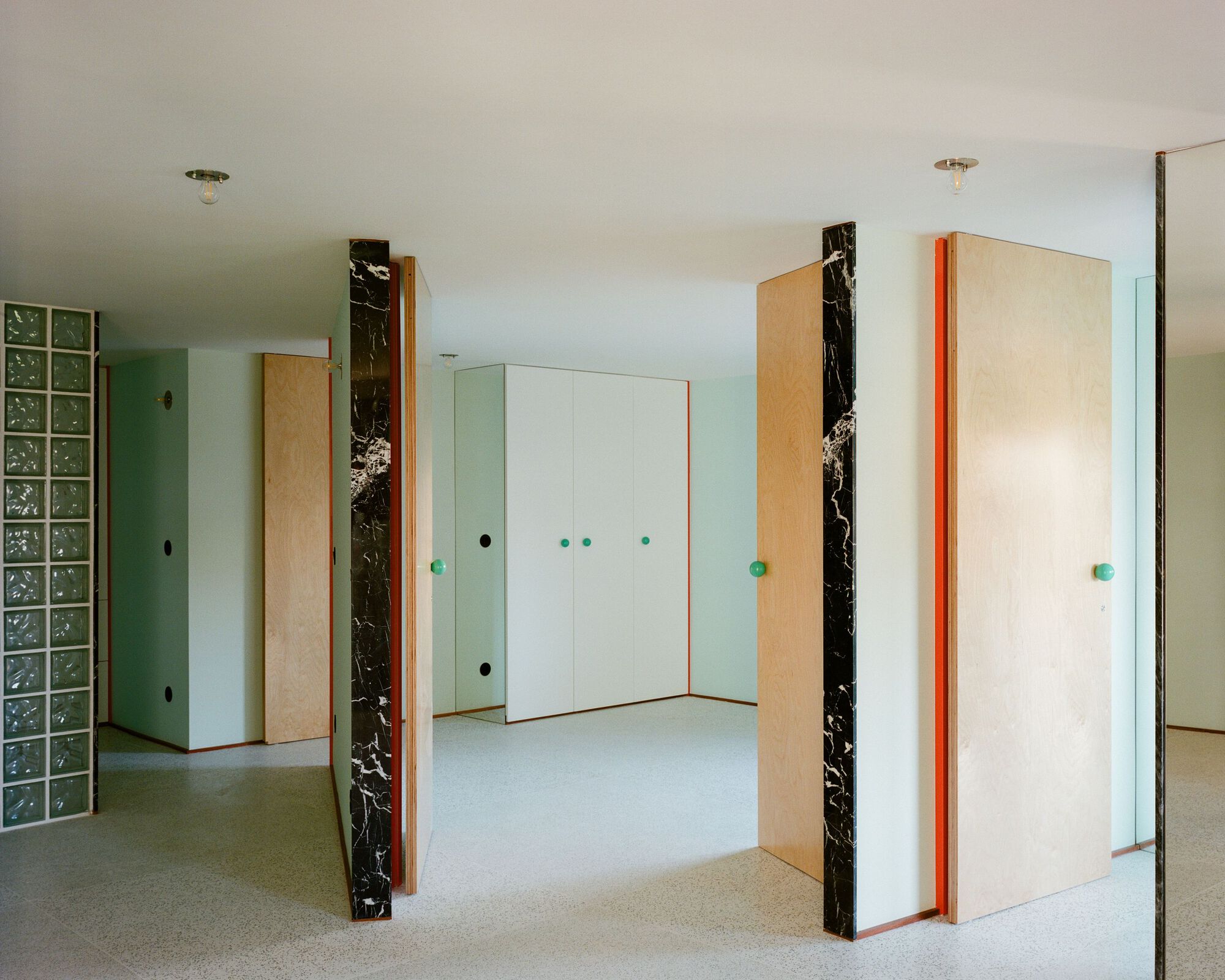 Interior space with pale-wood and black marble-clad doors, glass block wall, and turquoise door handles