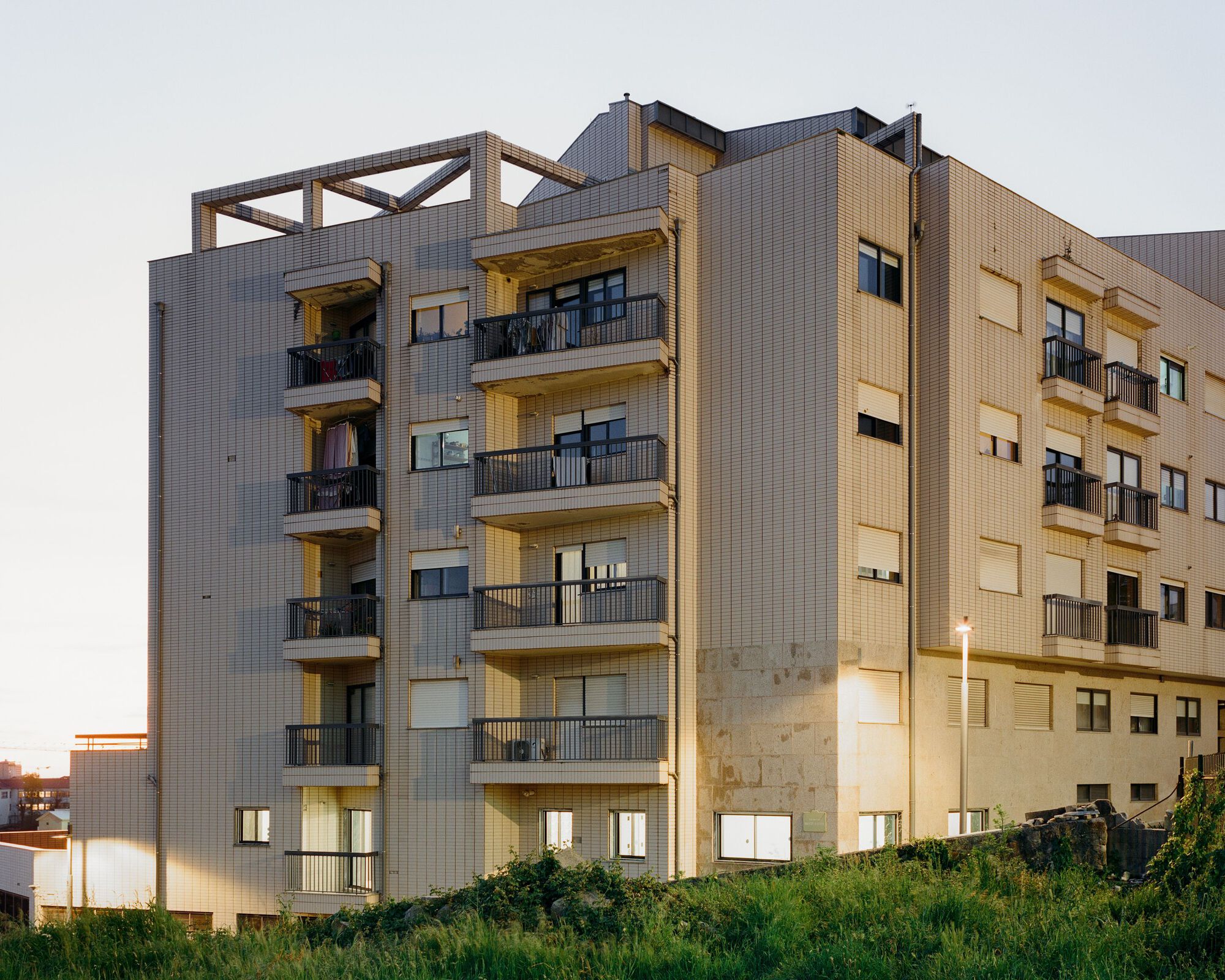 Facade of a multistory residential block with corrugated metal cladding and recessed balconies at dusk