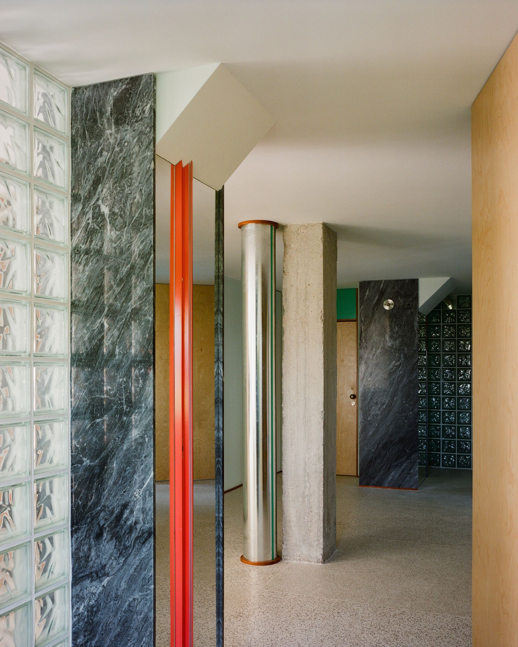 Entry hall with glass block wall, dark marble panels, orange metal trim, and cylindrical columns