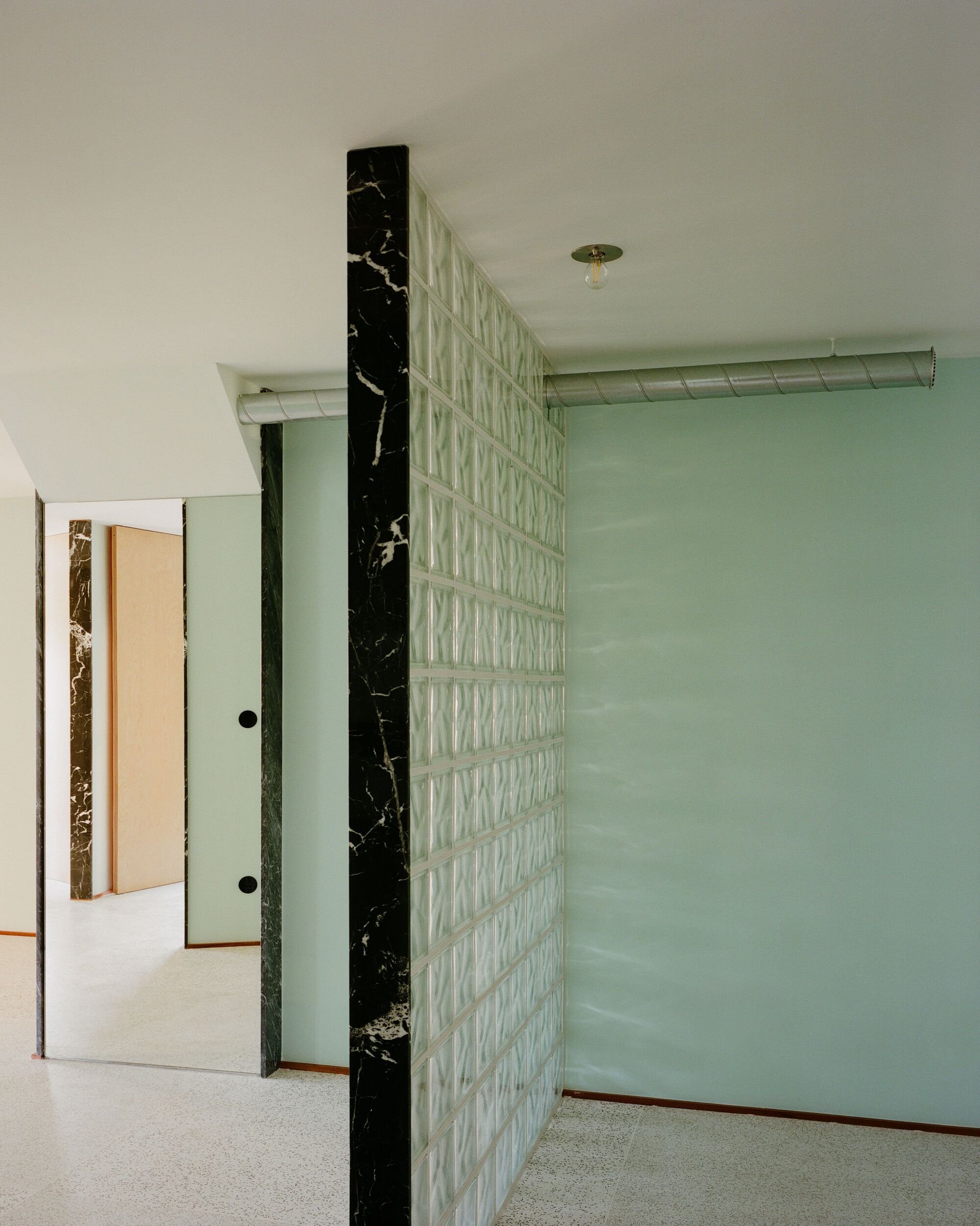 Translucent glass block partition wall with black marble column and pale green painted surfaces