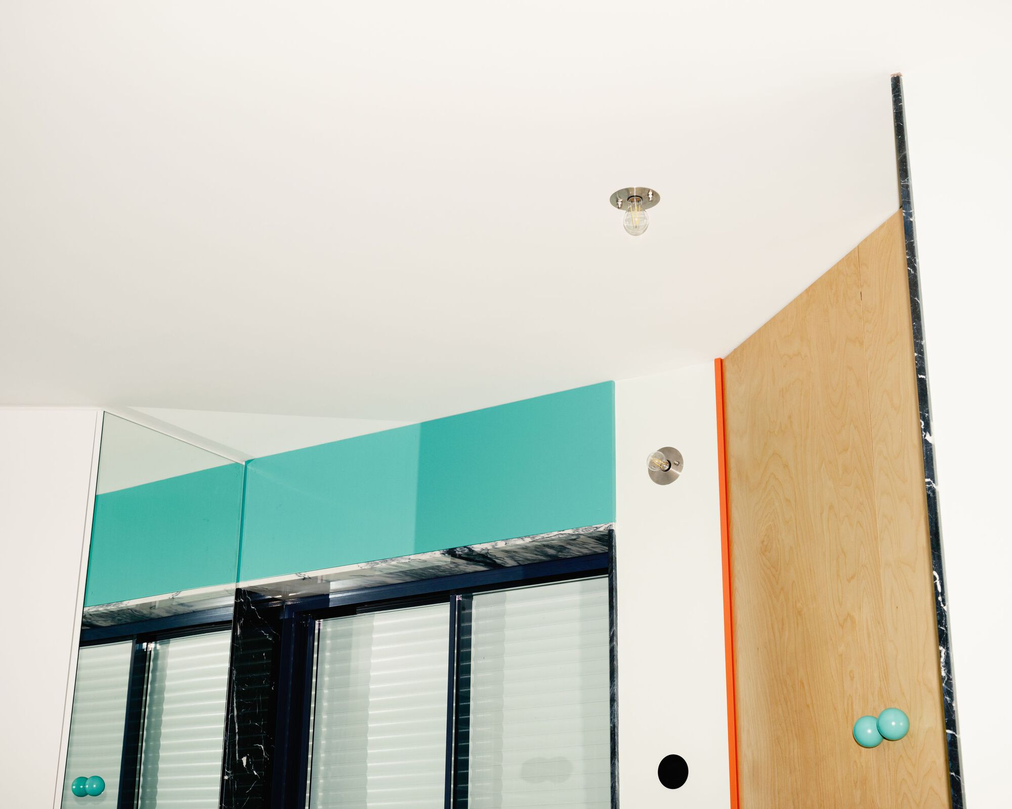 Corner detail showing plywood door with orange edge trim and blue knobs under a ceiling fixture