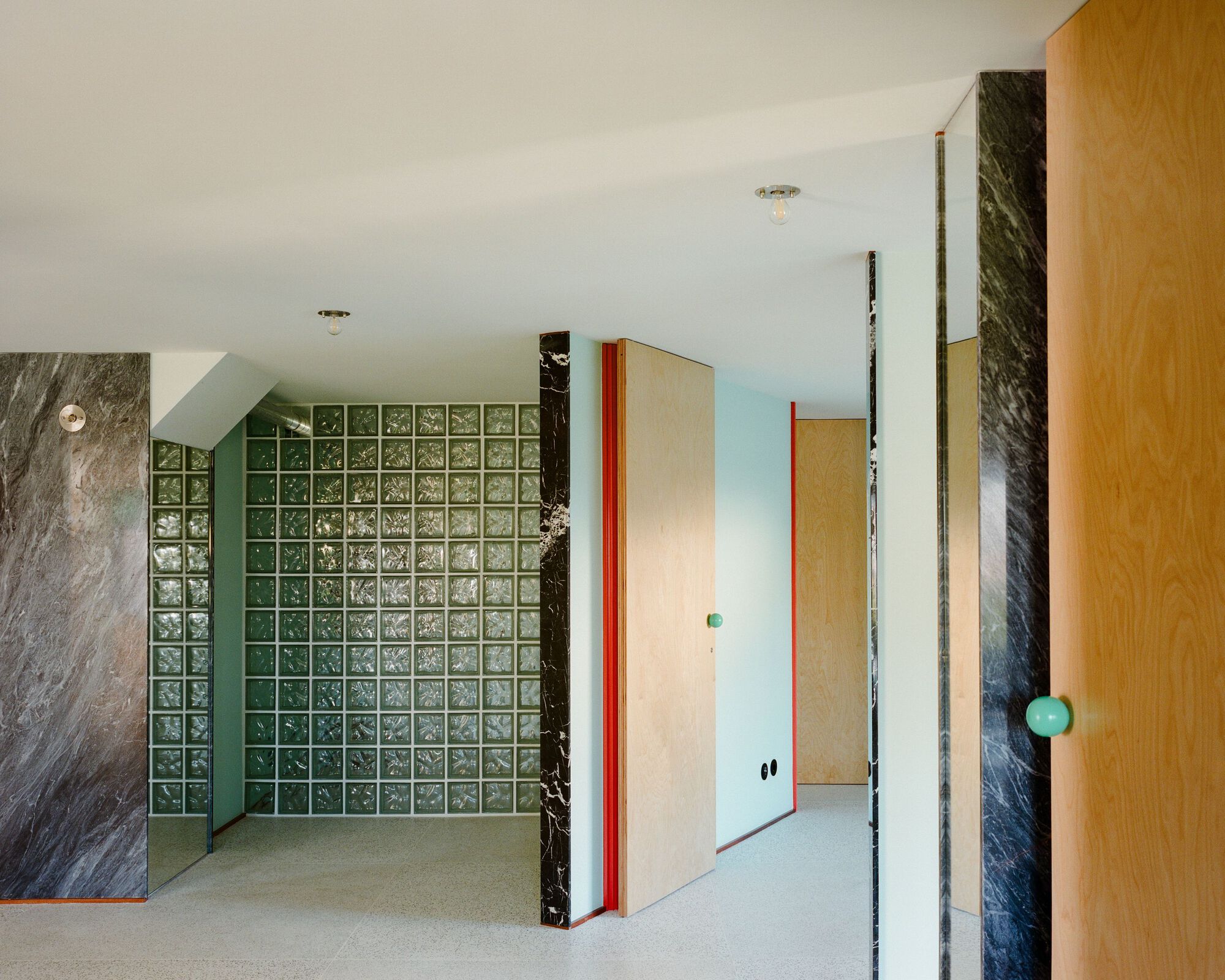 Interior passage with green glass block wall, light plywood doors, and black marble column surfaces