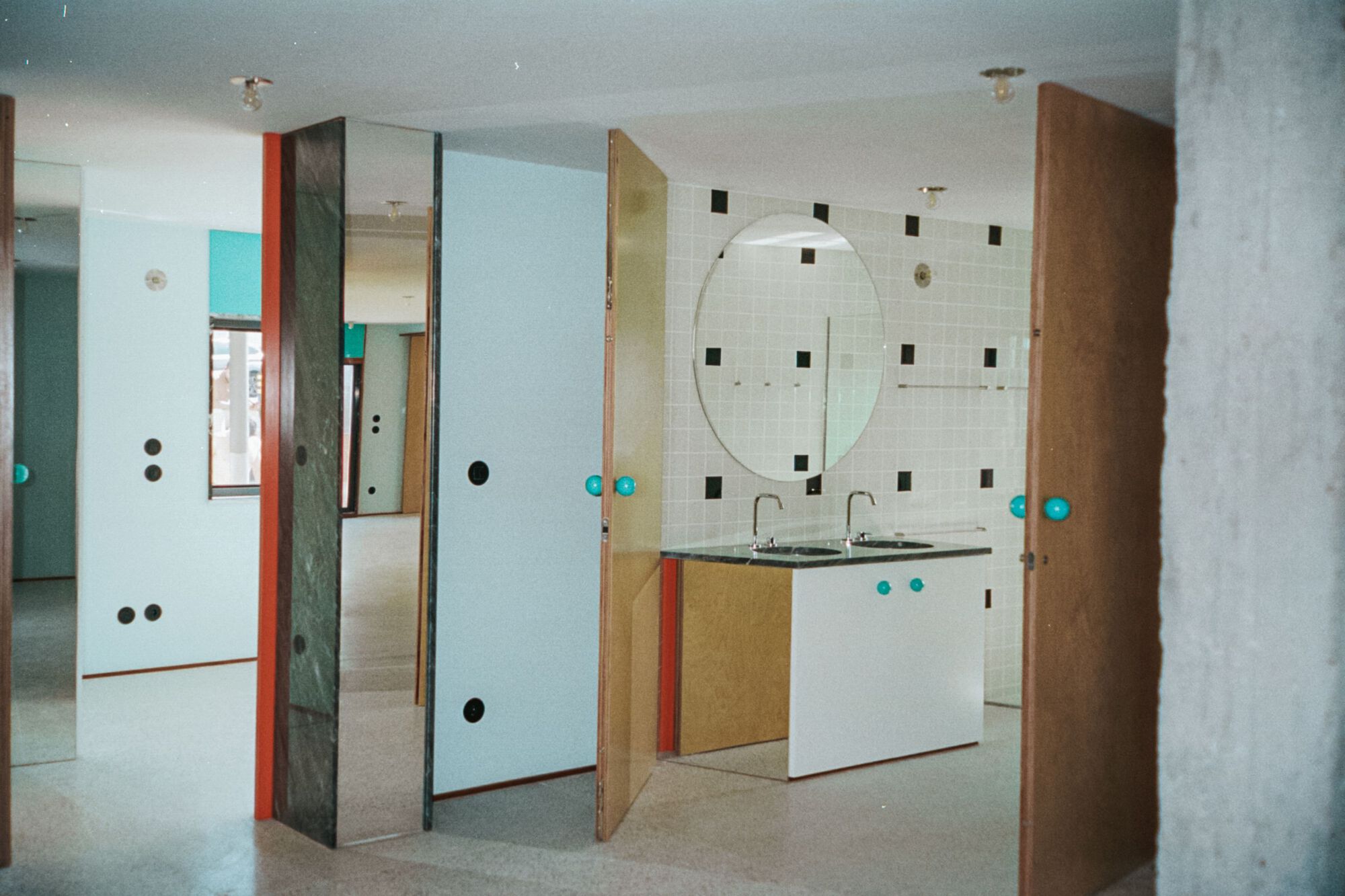 Open bathroom with freestanding tile partition walls, dual vanity and oval mirror above terrazzo floor