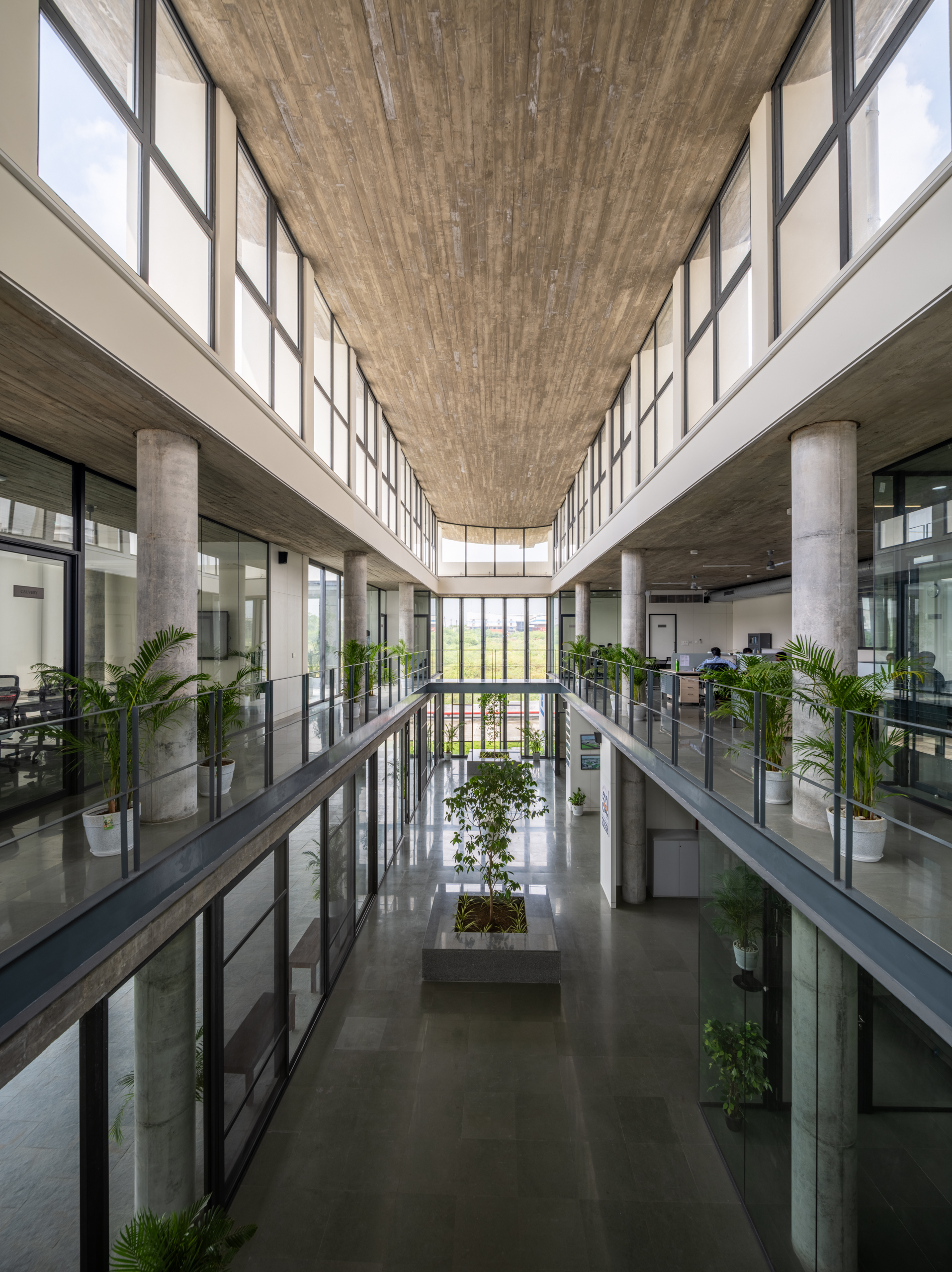 Three-story atrium with concrete ceiling, glazed galleries, circular columns and potted plants on railings