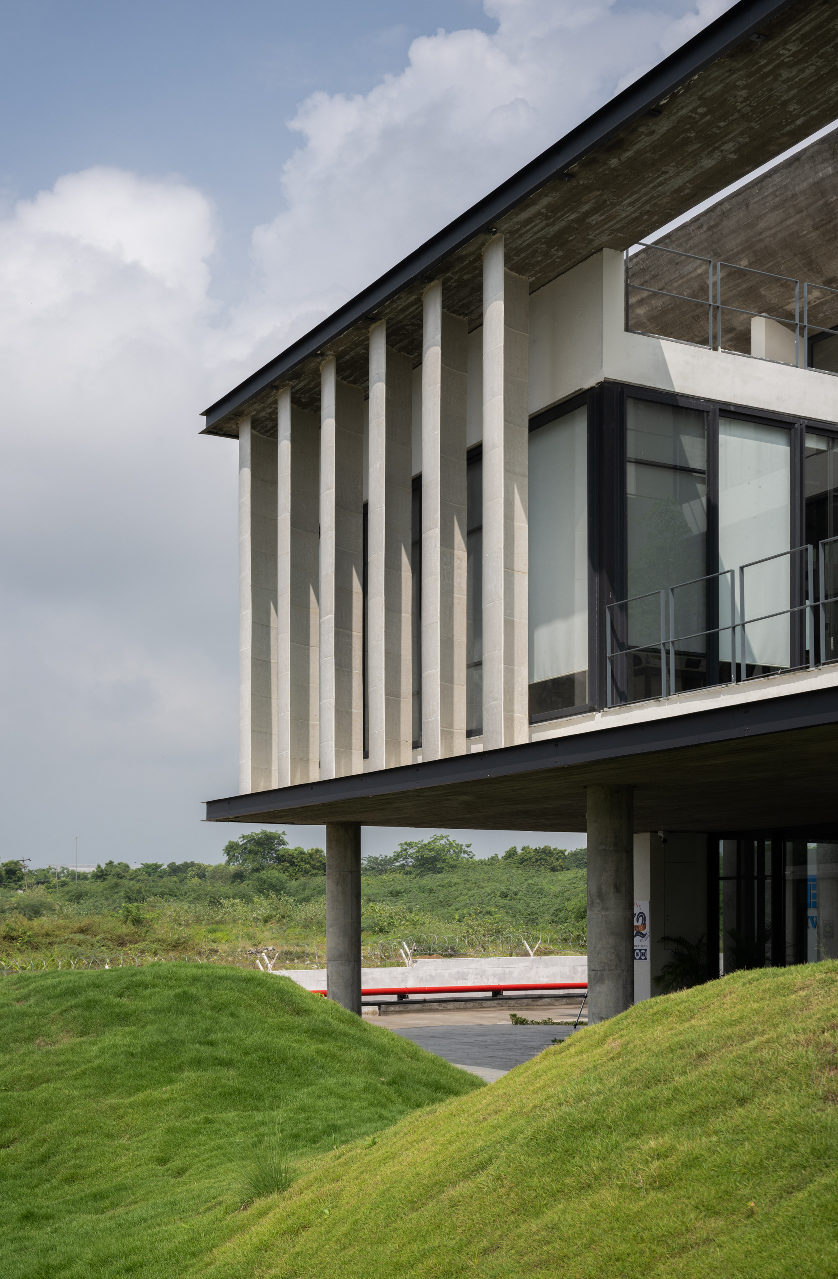 Cantilevered upper floor with vertical concrete fins above grass-planted berms under a partly cloudy sky