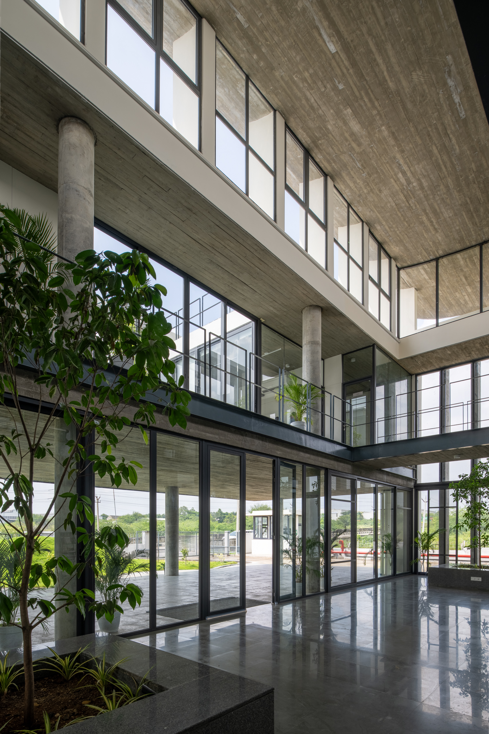 Double-height entry lobby with concrete columns, clerestory glazing, and potted trees flanking the entrance