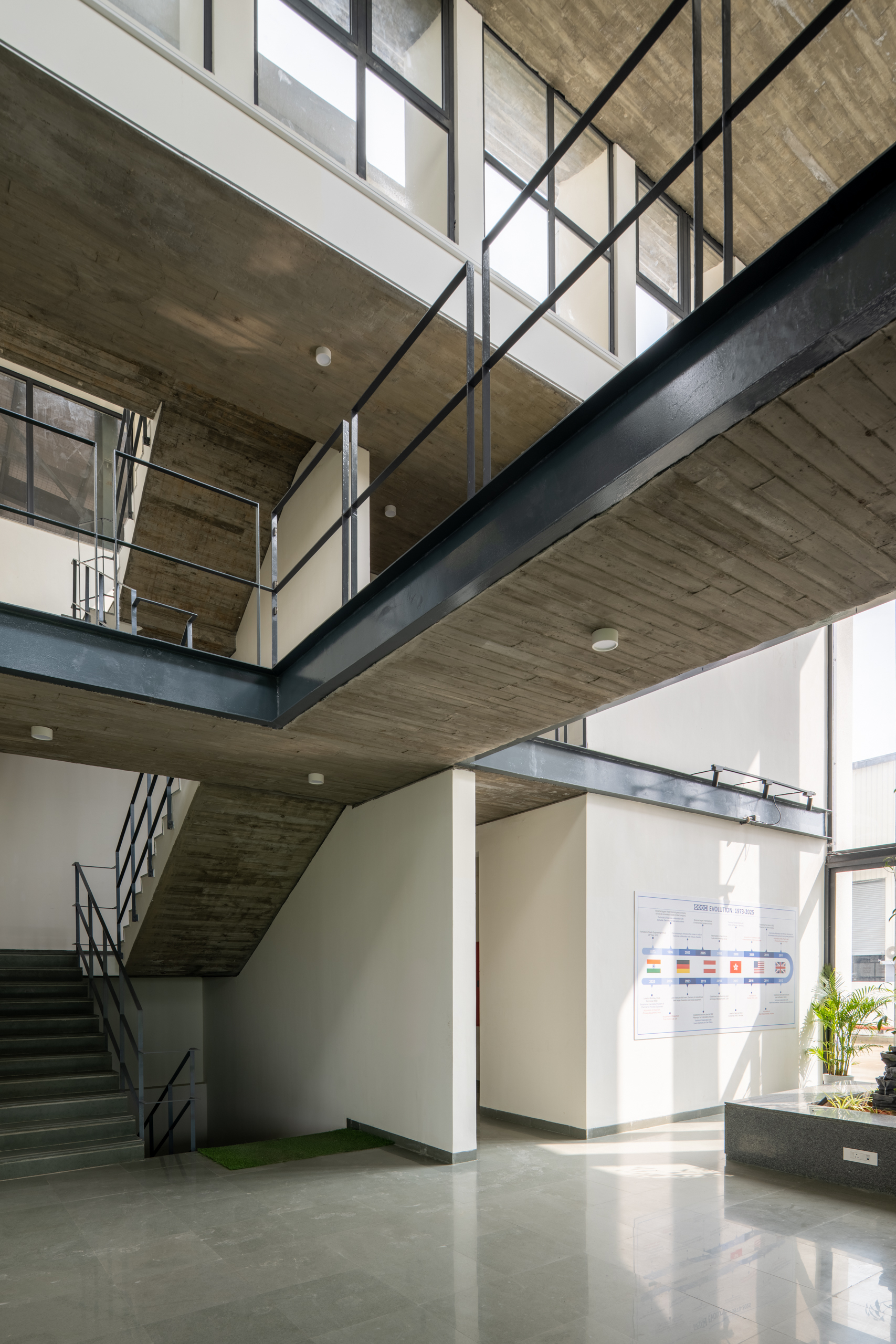 Interior atrium showing concrete soffit, steel stairs, and glass-railed mezzanine with informational wall panels