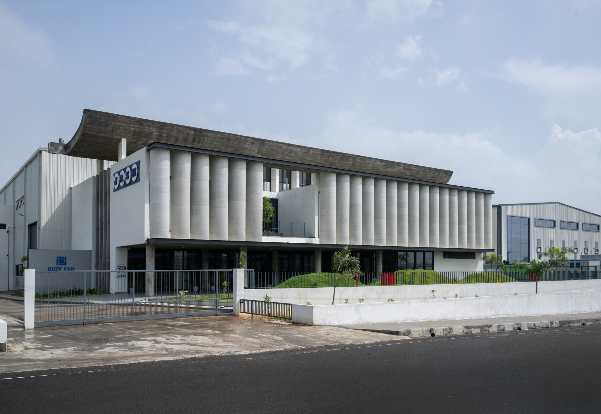 Street view of the ribbed concrete facade with flat roof canopy and landscaped foreground
