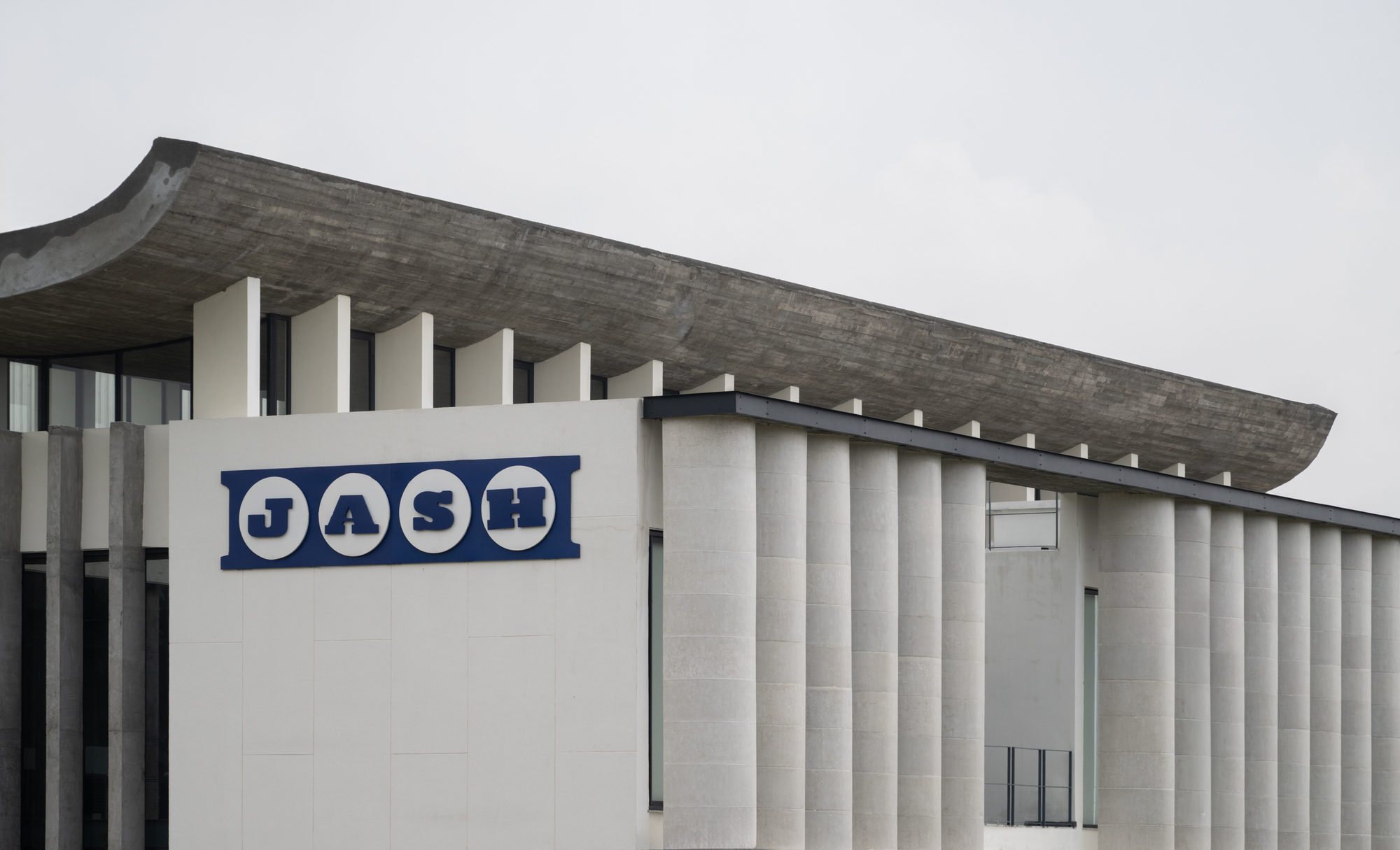 Close-up of the signage panel against the vertical ribbed concrete facade under grey sky