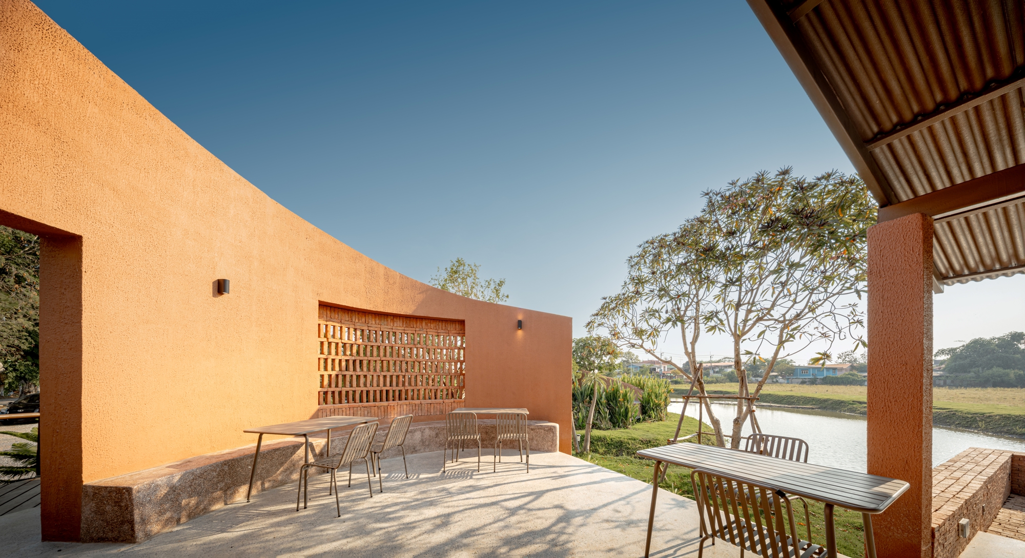Terrace with perforated brick screen wall framing views of a mature tree and water body