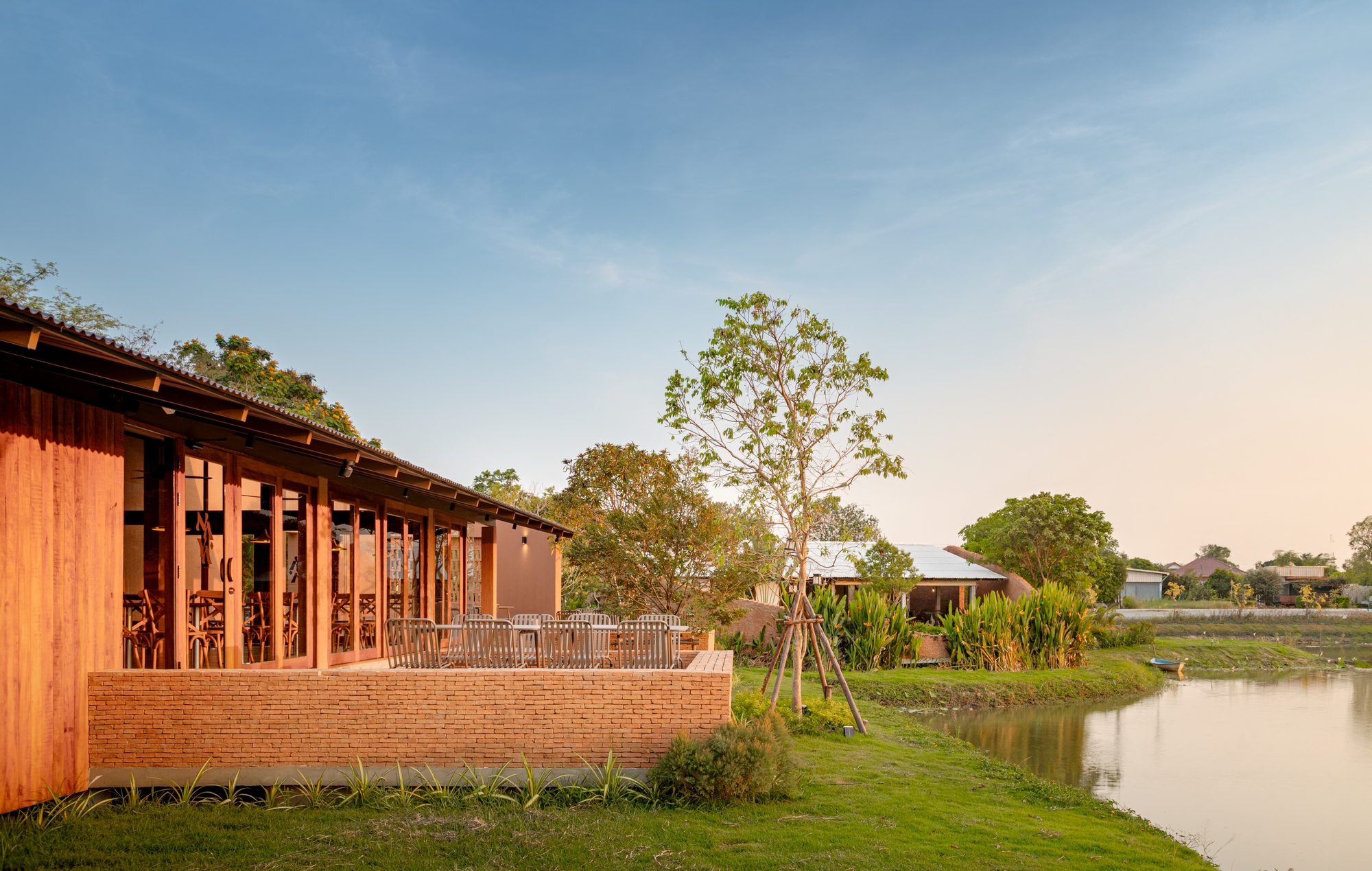 Timber-screened pavilion with brick base along a pond edge in golden afternoon light