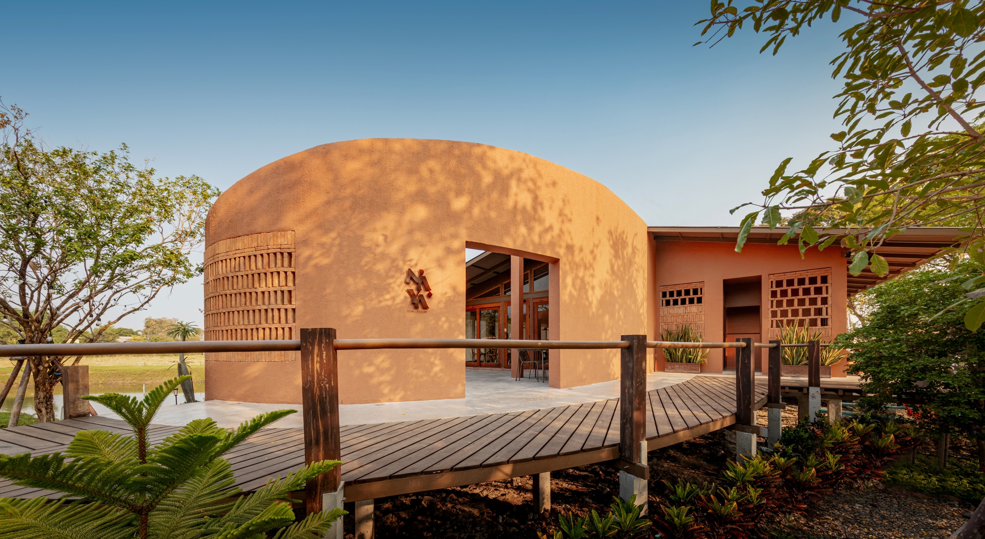 Curved terracotta vault with lattice openings accessed by a timber boardwalk through planted beds