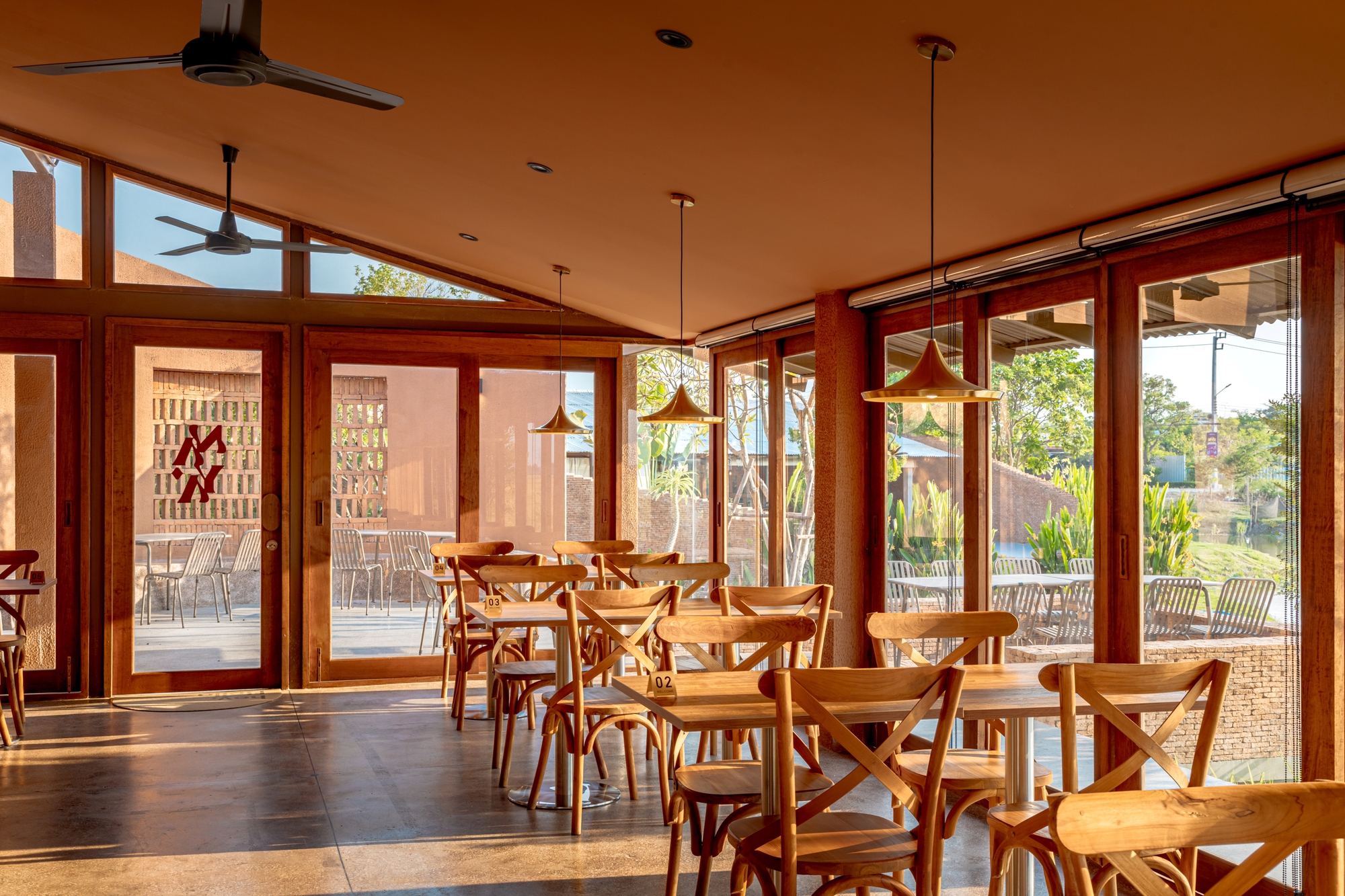 Dining hall interior with timber-framed glazing, pendant lights, and terracotta-painted ceiling