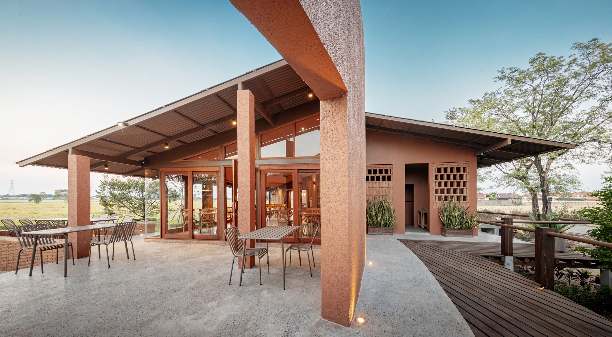 Covered terrace with exposed timber roof beams and textured columns overlooking open grassland at dusk