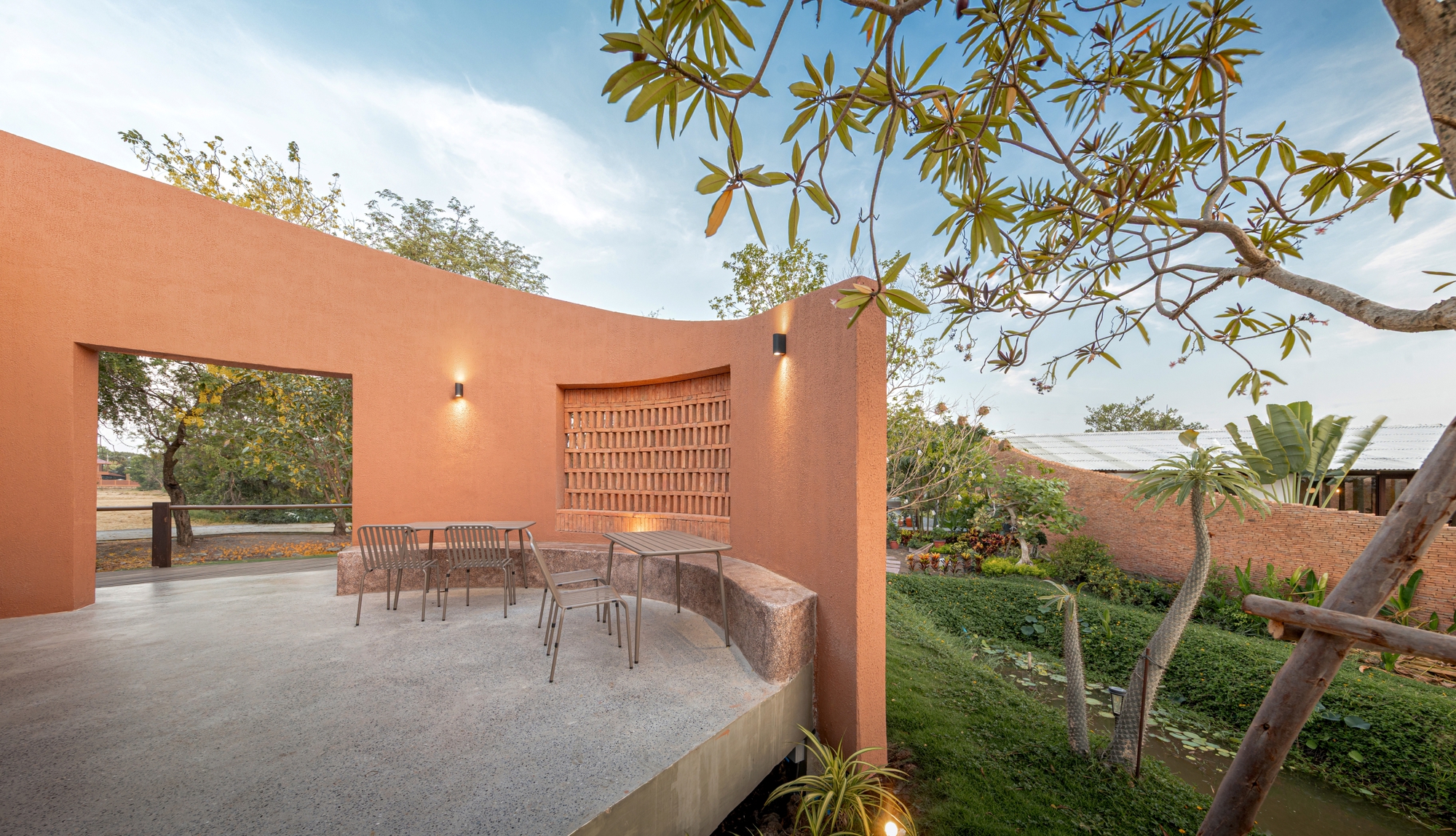Outdoor terrace with latticed brick screen and framed view to the landscape under a plumeria tree
