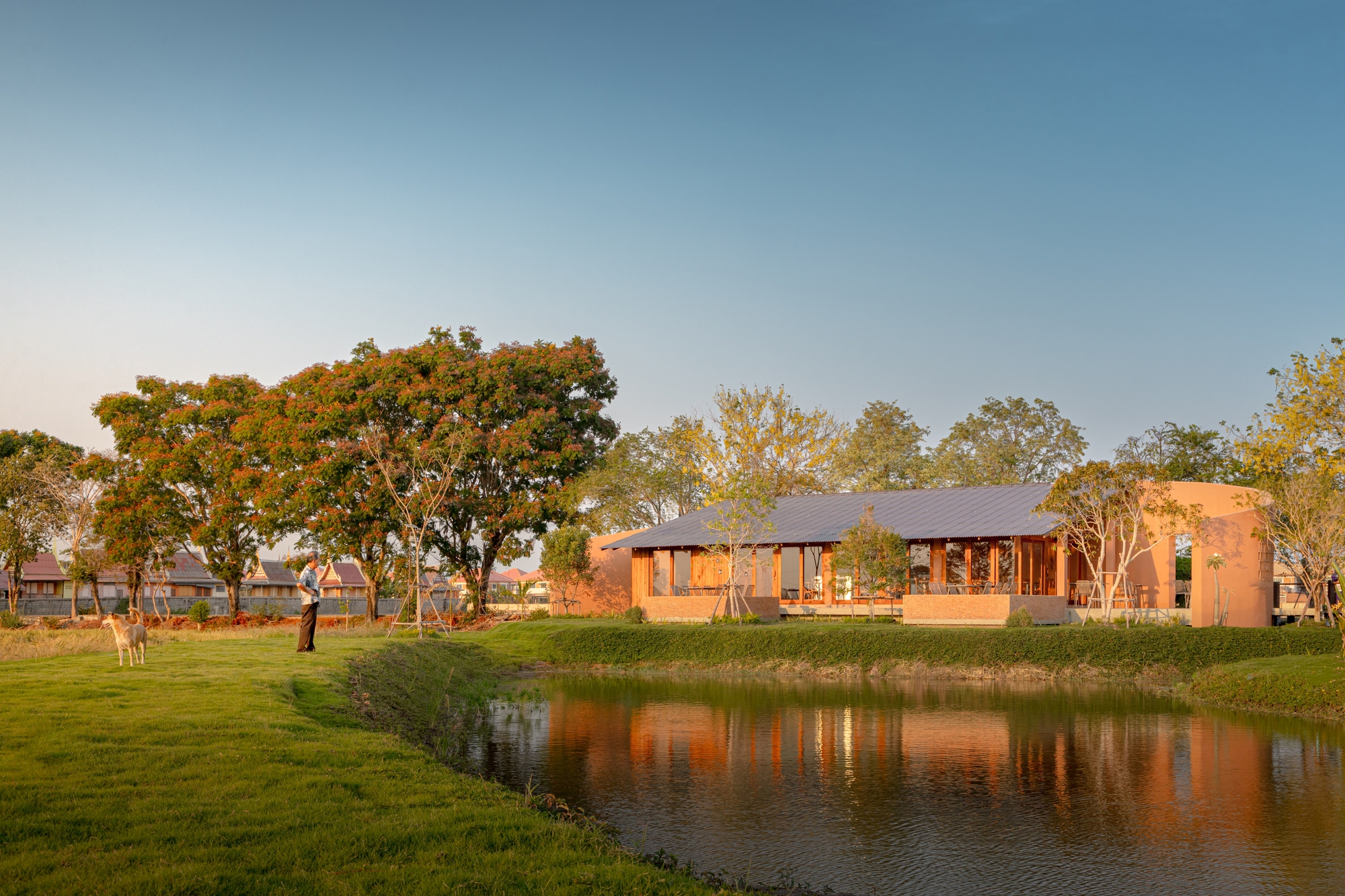 Long view across a reflecting pond toward the terracotta pavilions nestled among mature trees at golden hour