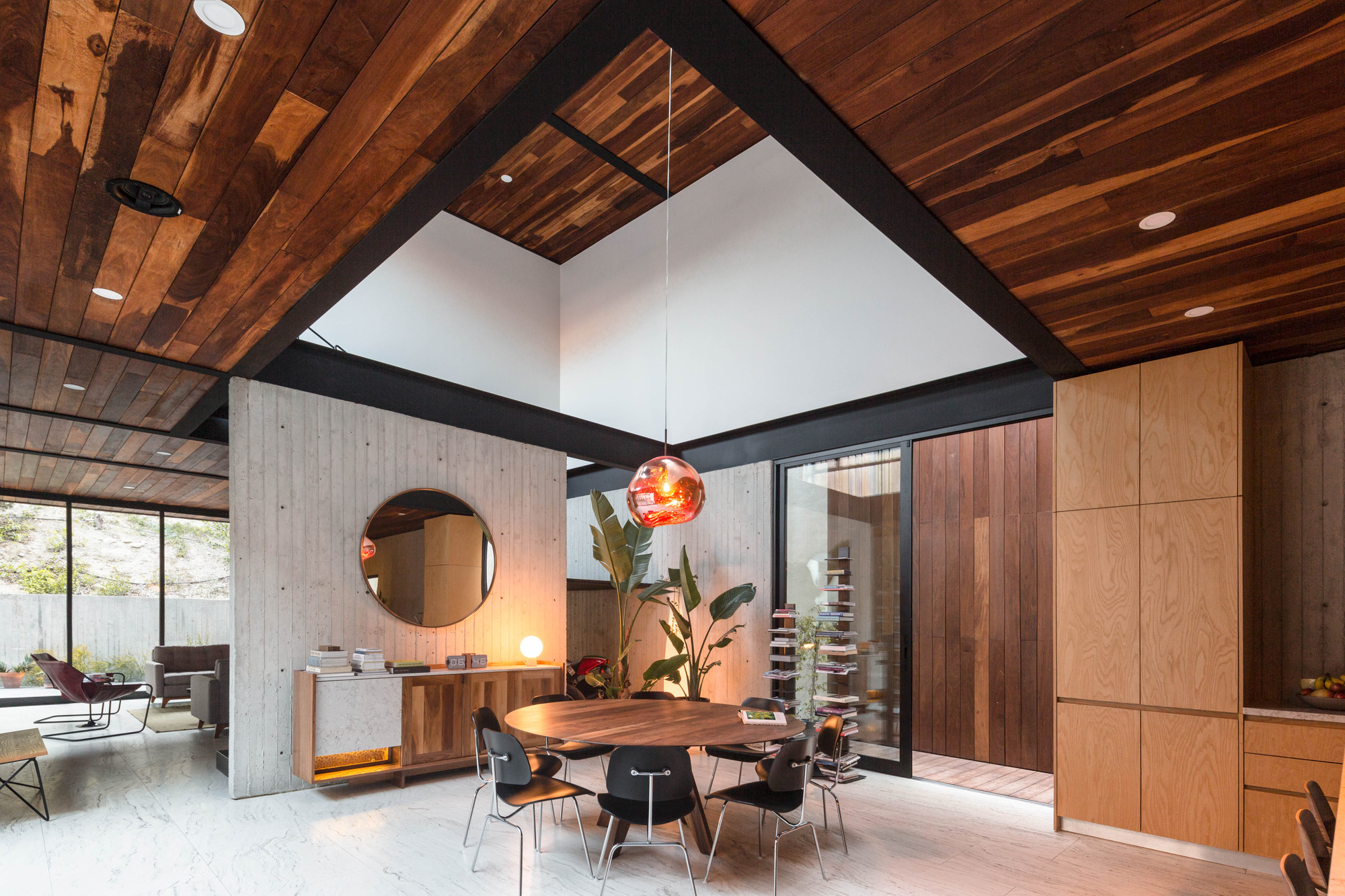 Dining area under a timber ceiling with steel beams, a round walnut table and a copper pendant lamp