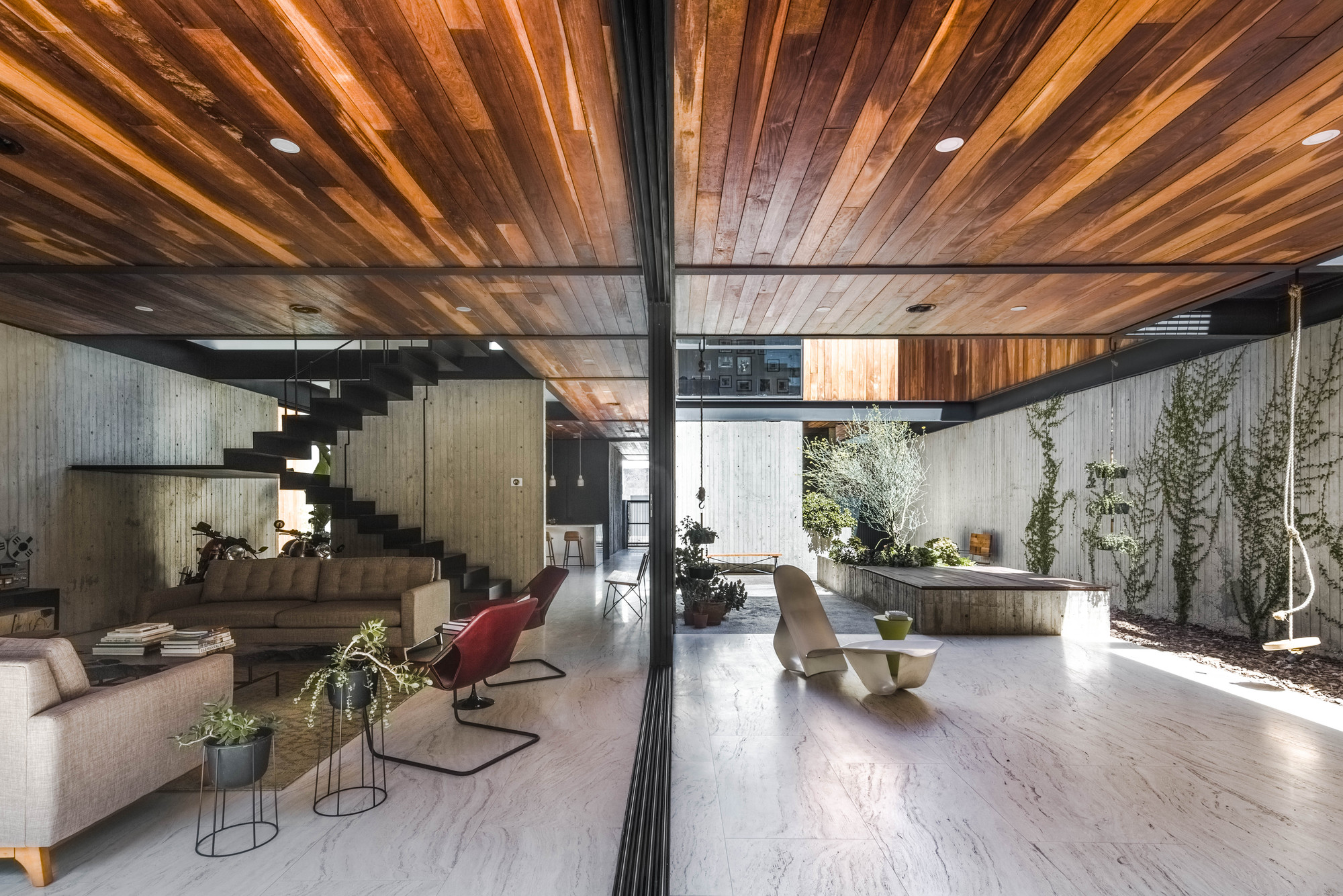 Living space opening through sliding glass to a courtyard with climbing plants, a rope swing and a floating steel stair