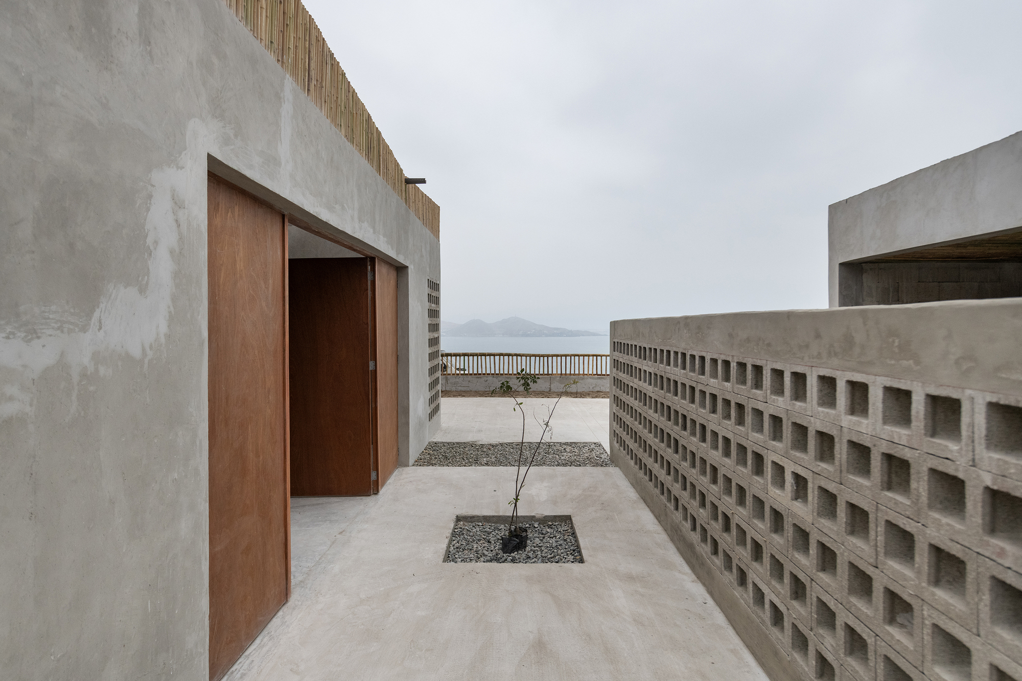 Concrete courtyard passage with timber doors and perforated screen wall framing distant mountains