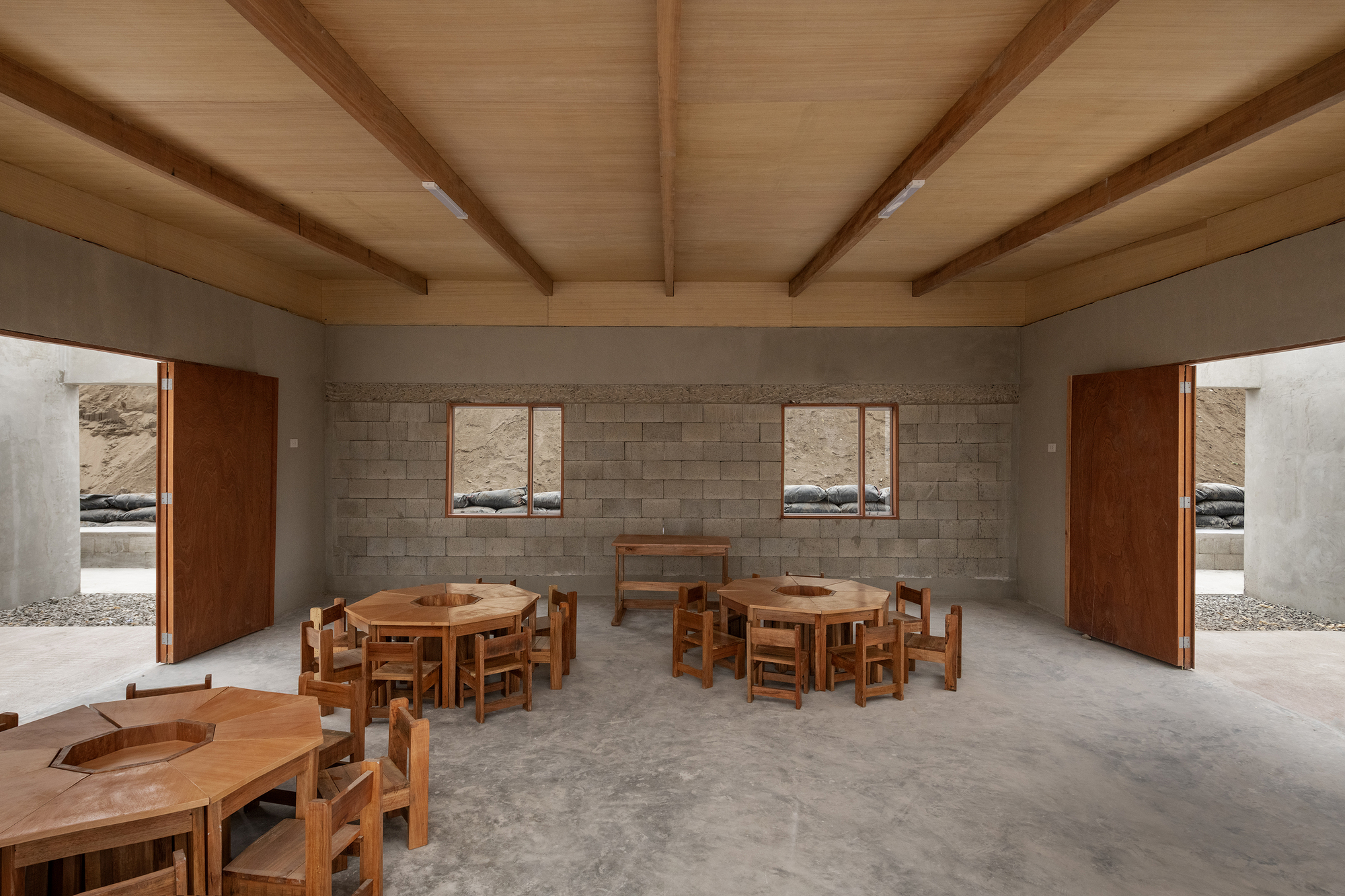 Interior space with exposed timber ceiling beams and round wooden tables beneath block wall windows