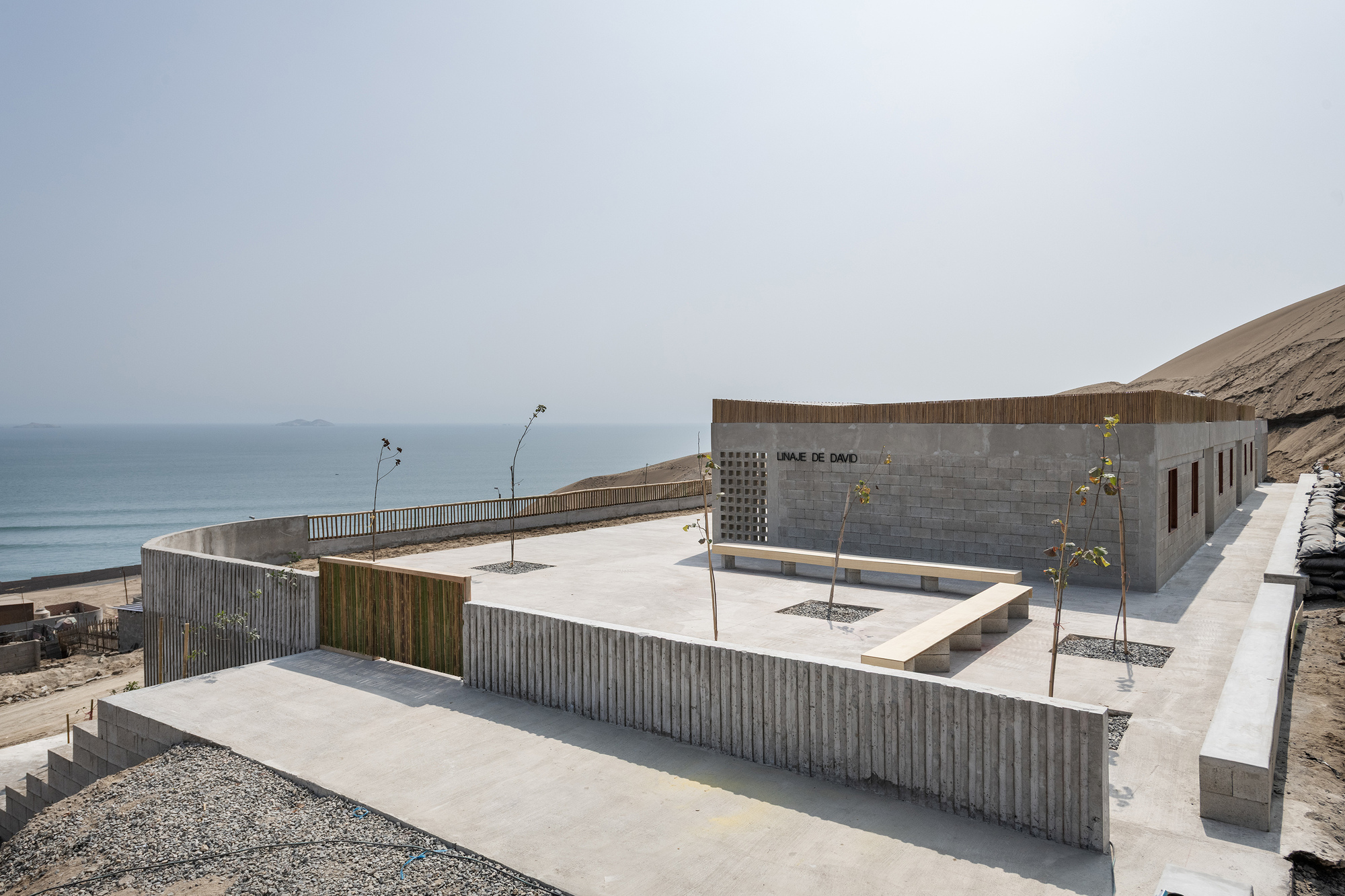 Elevated courtyard with timber-clad walls and young trees in gravel beds overlooking the coastline