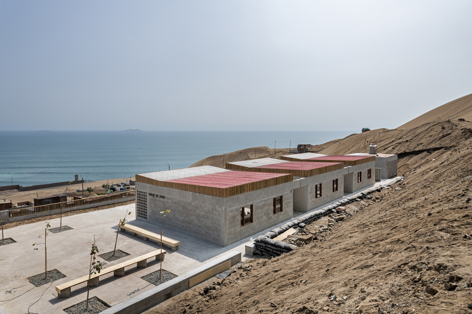 Side view of the concrete block building with pink roof panels and timber parapet on a hillside