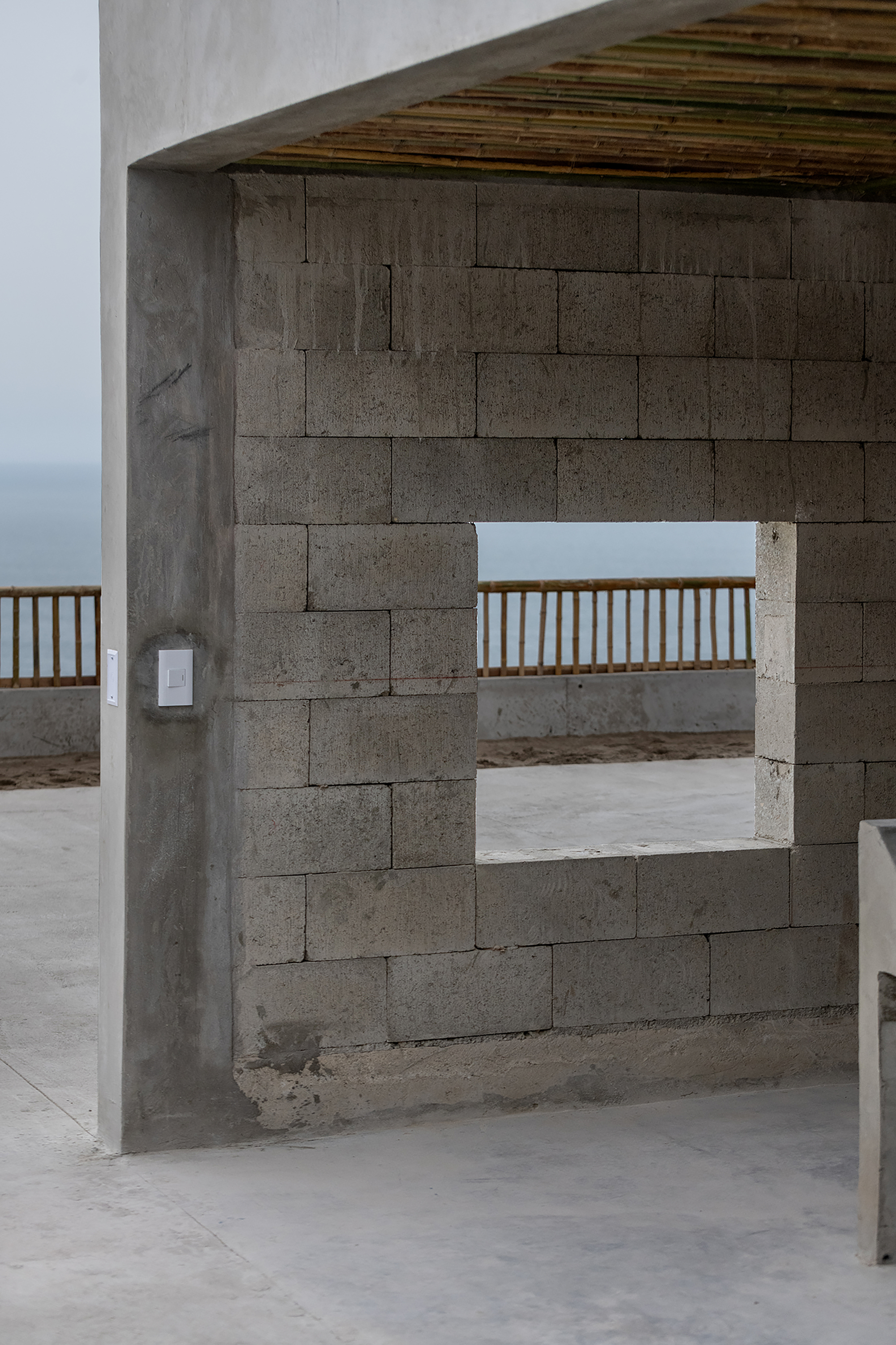 Concrete block wall with square opening framing a timber railing and the ocean horizon beyond