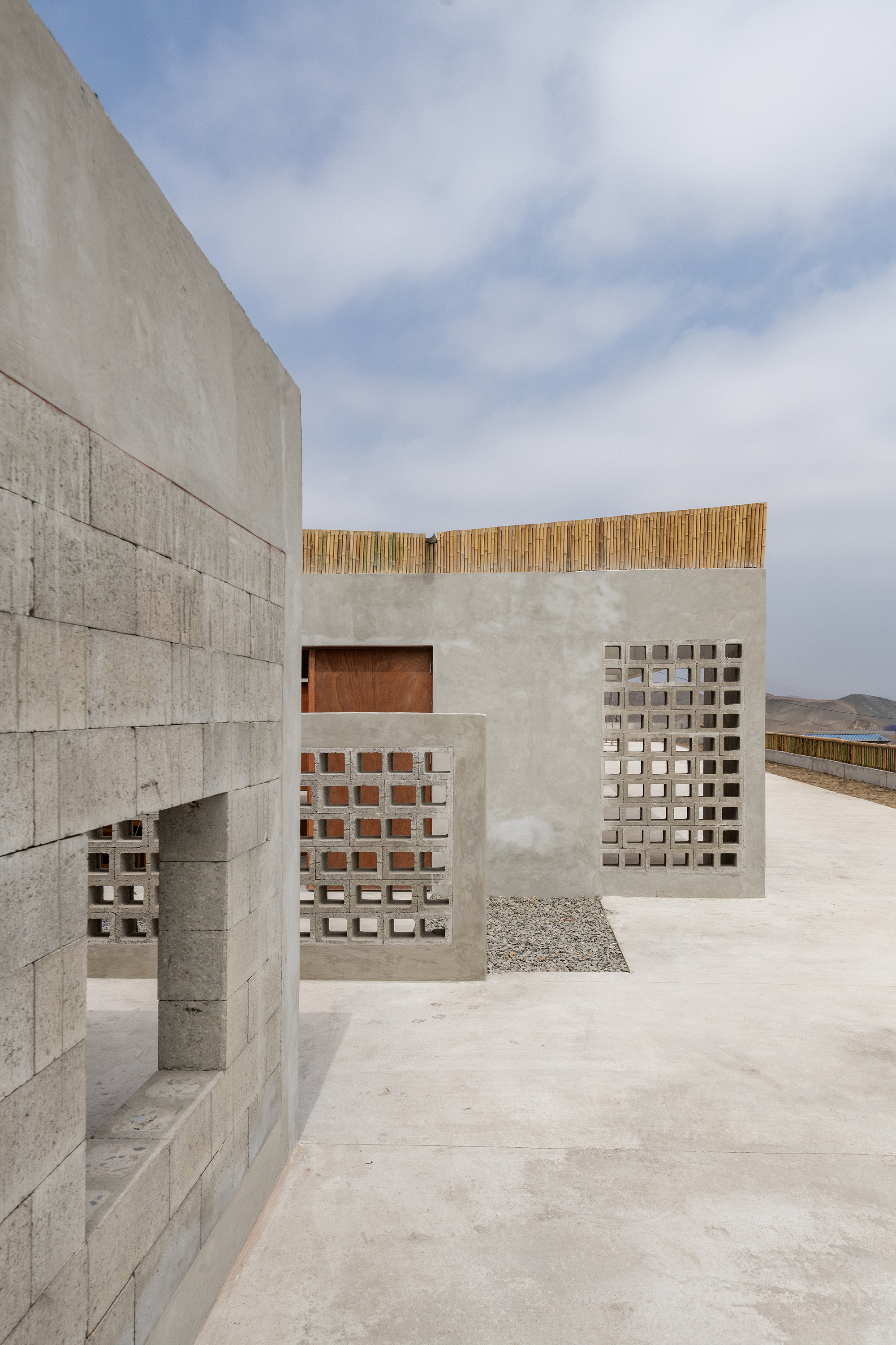 Concrete block walls with perforated screens and timber coping under a cloudy sky