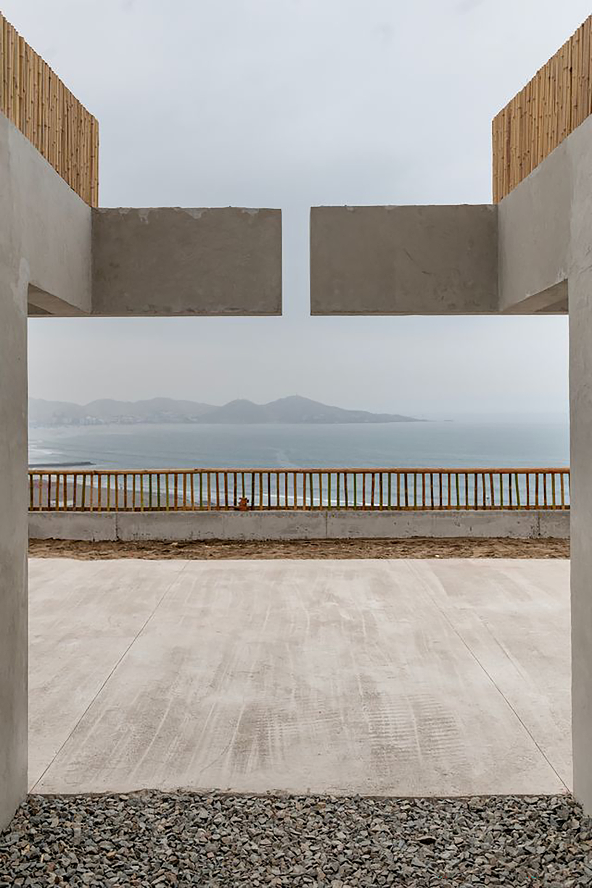 Concrete portal framing a timber railing and distant coastal mountains across the water