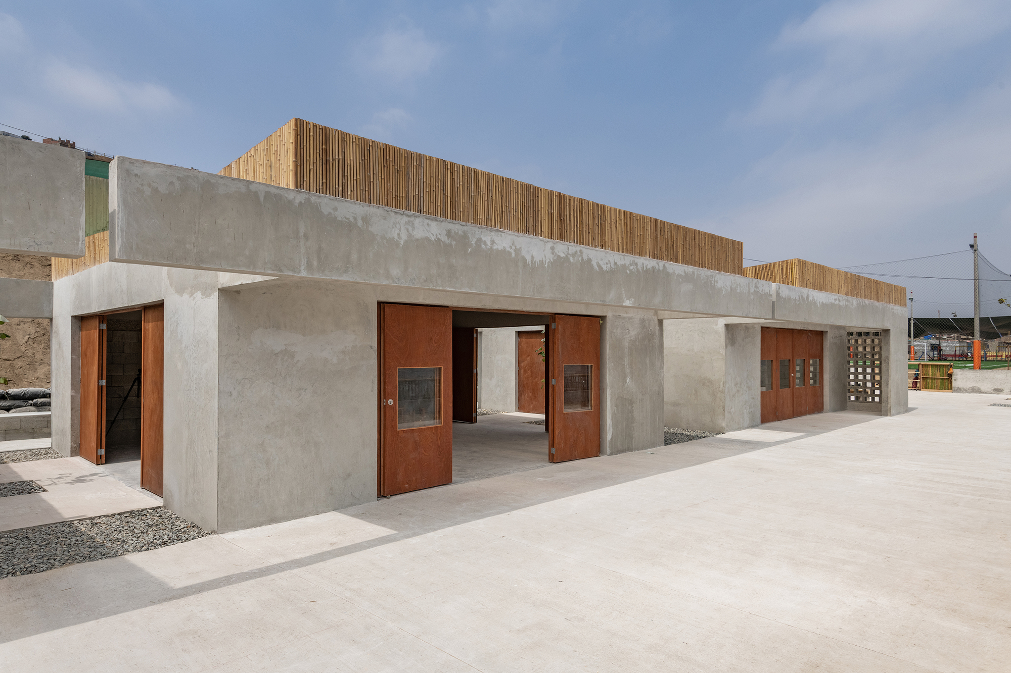 Linear concrete pavilion with vertical timber screen above and rusted steel doors along the facade