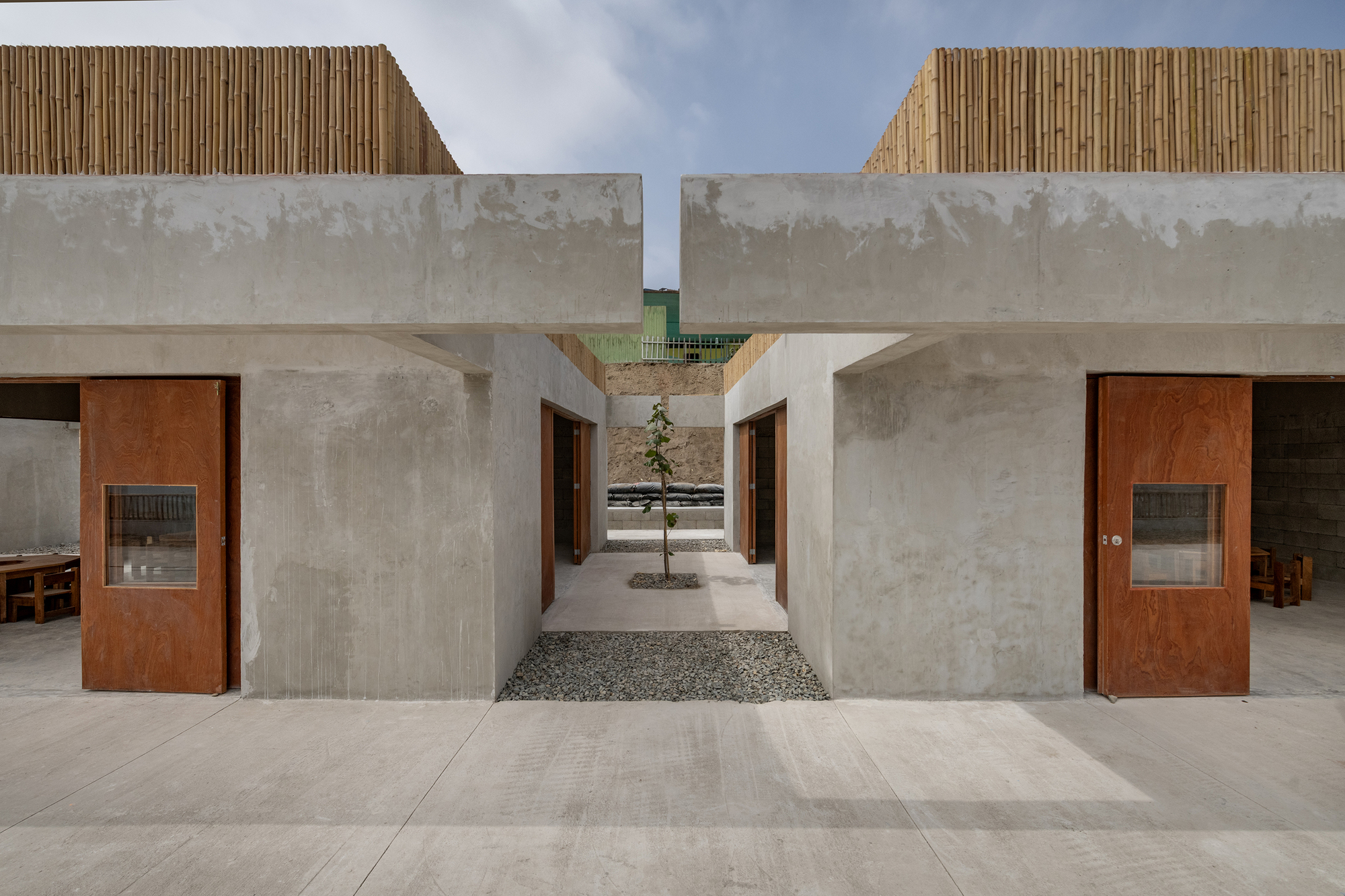 Courtyard passage between concrete volumes with a single tree and gravel ground surface