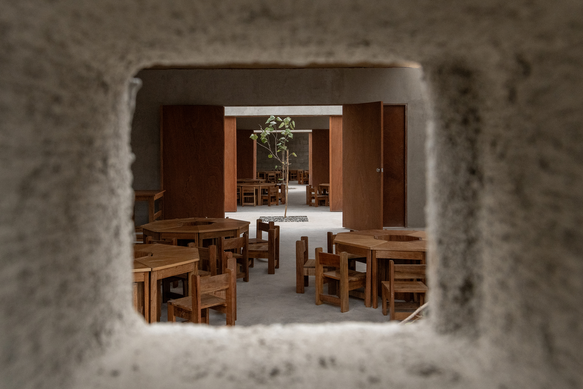 View through concrete block window opening to timber furniture and aligned doorways beyond