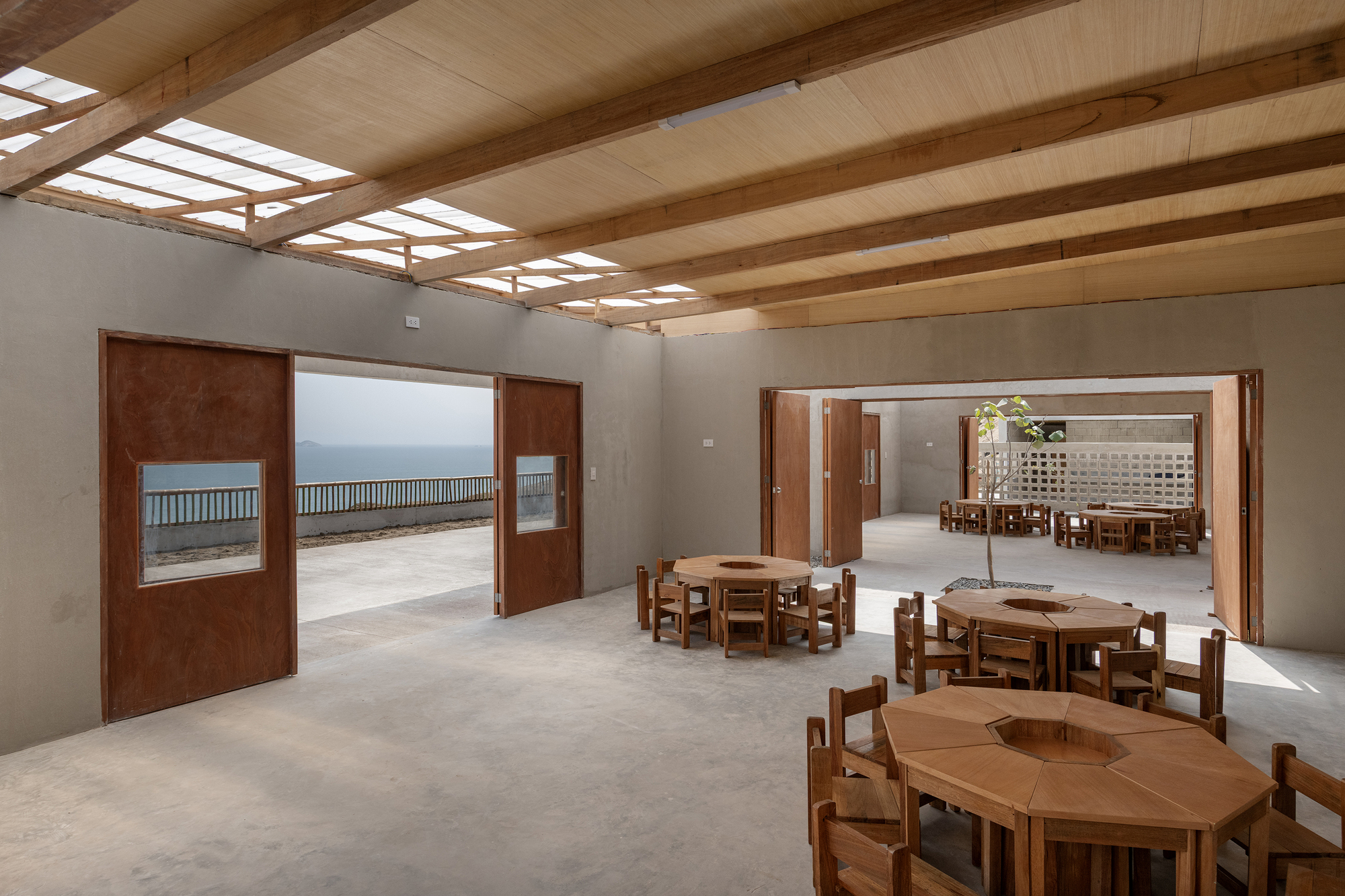 Interior view through open rusted steel doors connecting classrooms with exposed timber roof structure