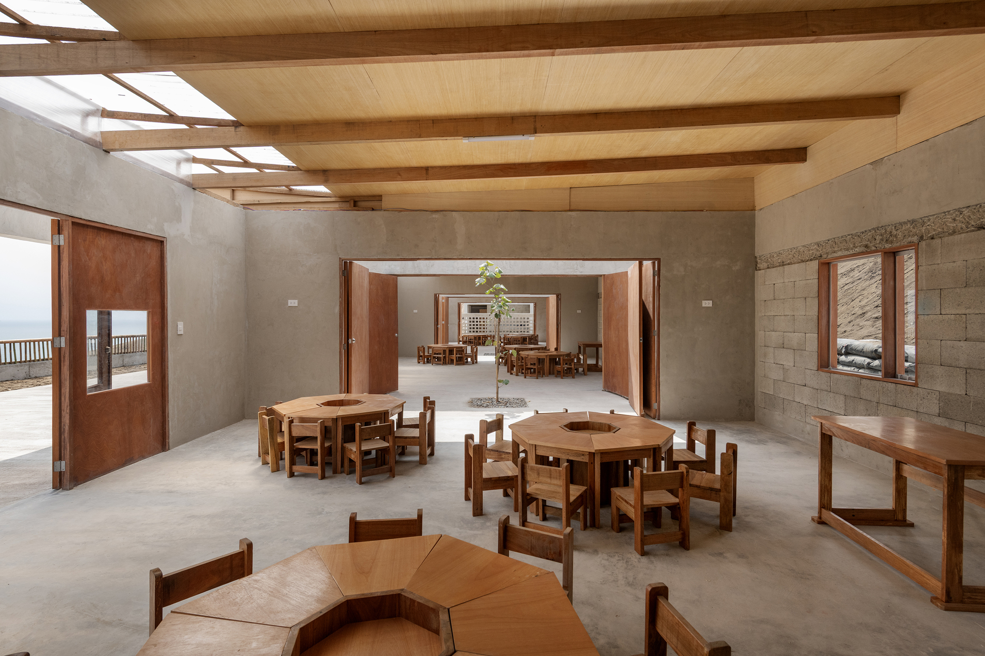 Interior dining hall with exposed timber beams, concrete block walls, and wooden furniture arranged under skylights