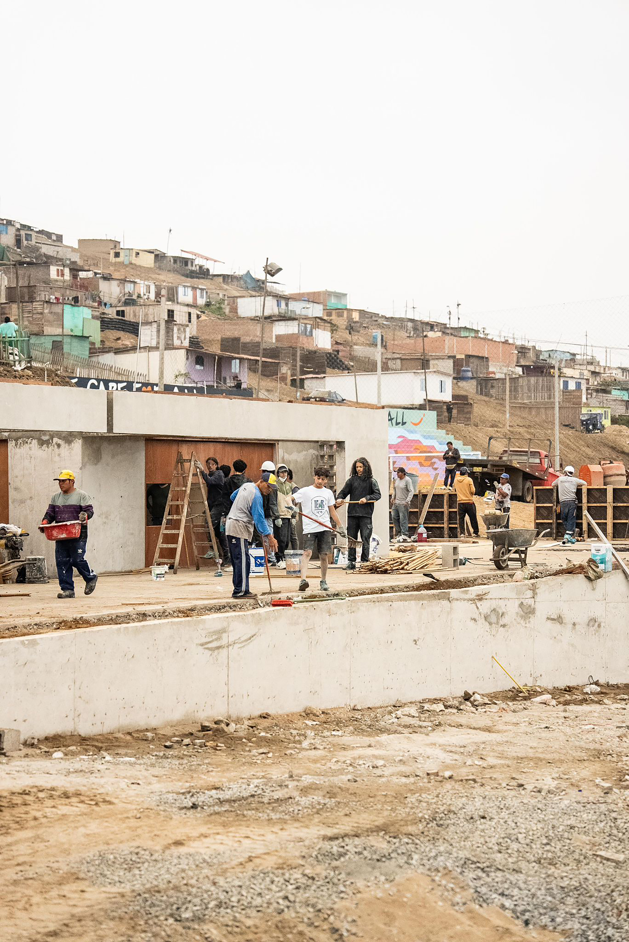 Construction site with workers assembling formwork on a hillside neighborhood in the background