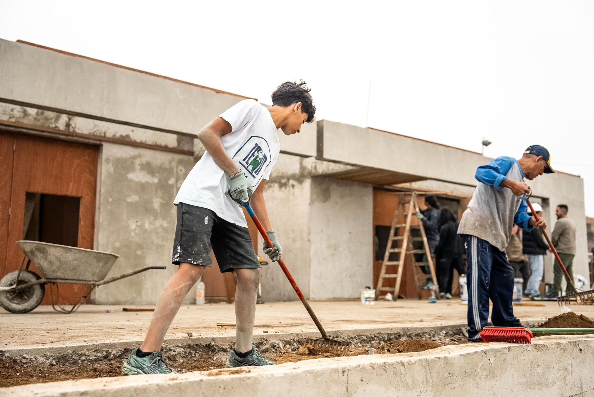 Workers raking gravel on a concrete foundation slab during construction