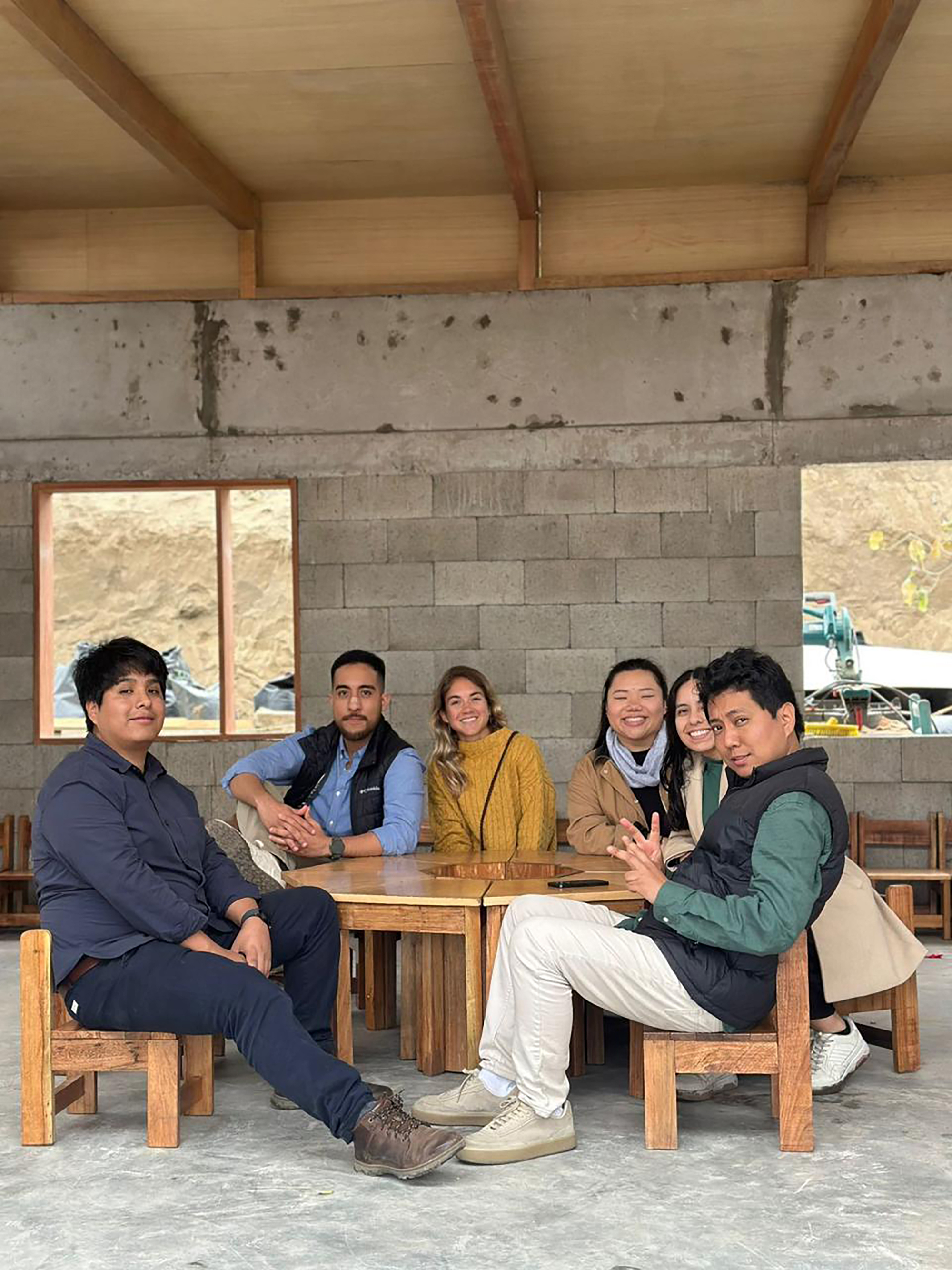 Group seated at a wooden table in a space with concrete block walls and plywood ceiling