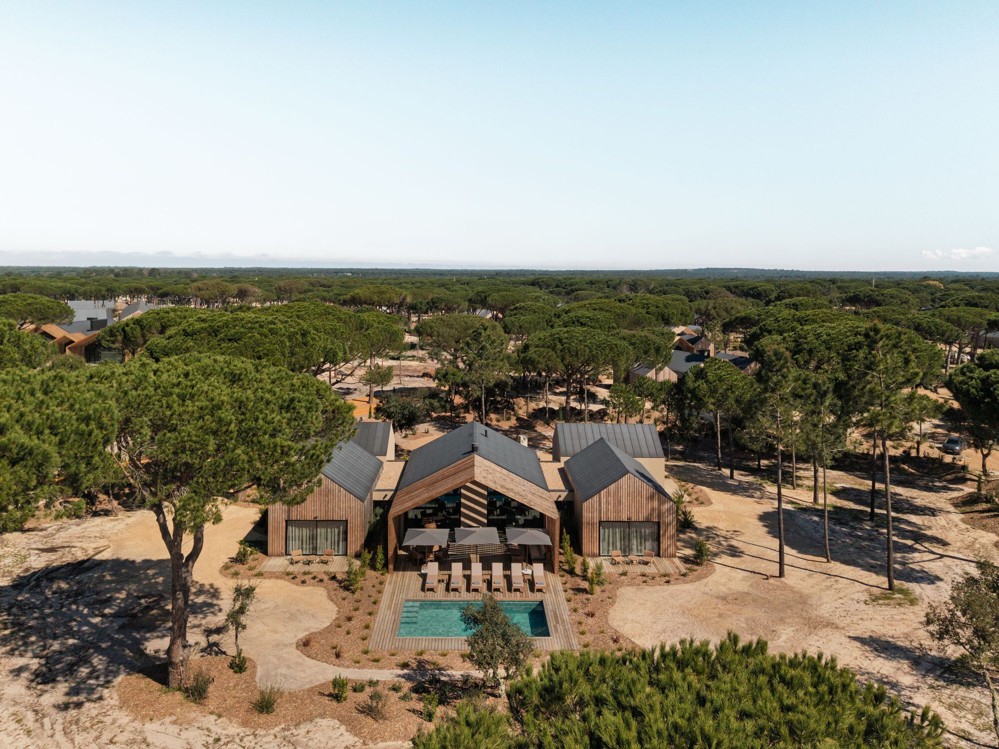 Aerial view of the compound showing three gabled volumes arranged around a central courtyard with pool and deck