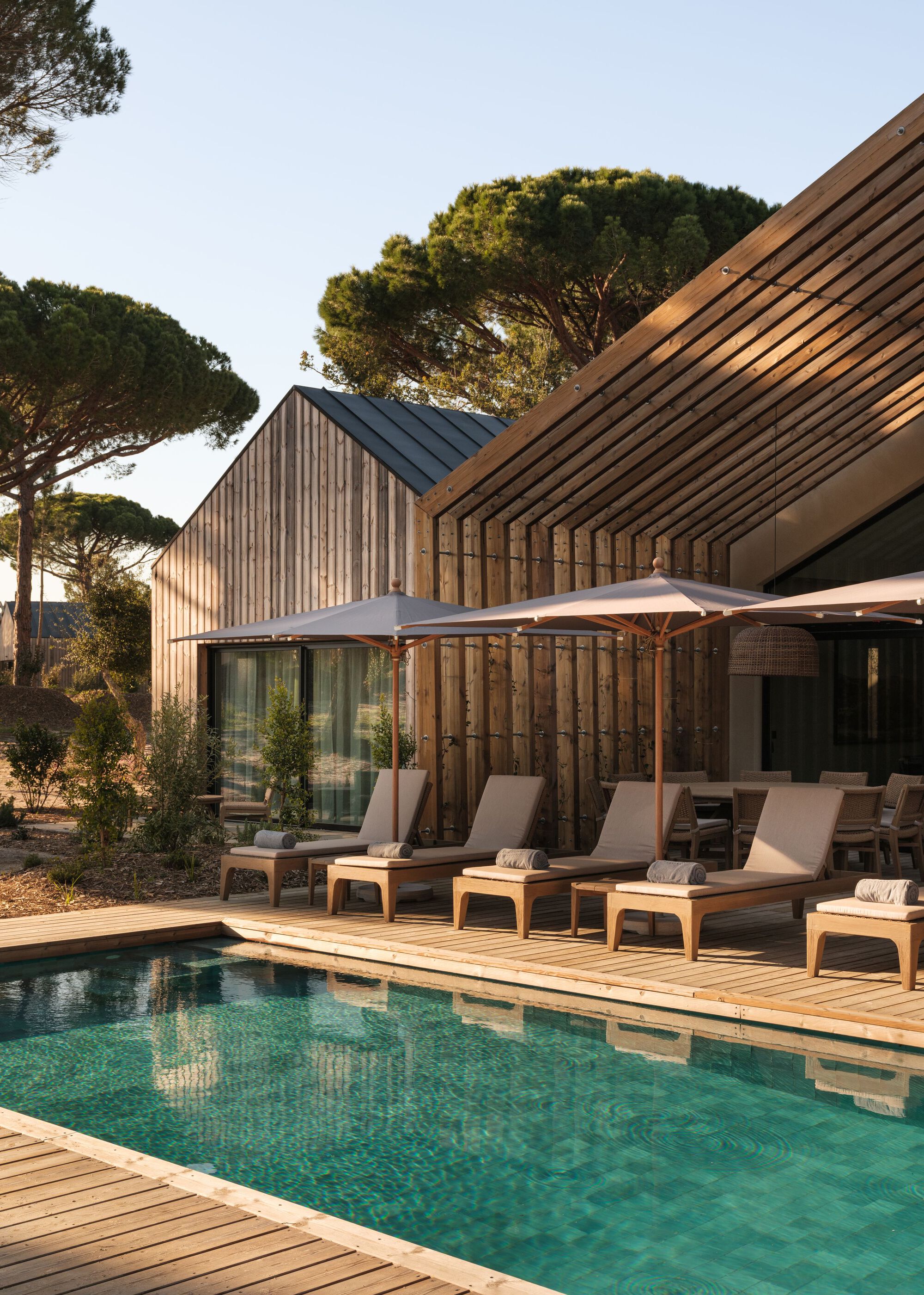 Timber deck with lounge chairs and white umbrella alongside the pool at dusk beneath the vertical-clad gables