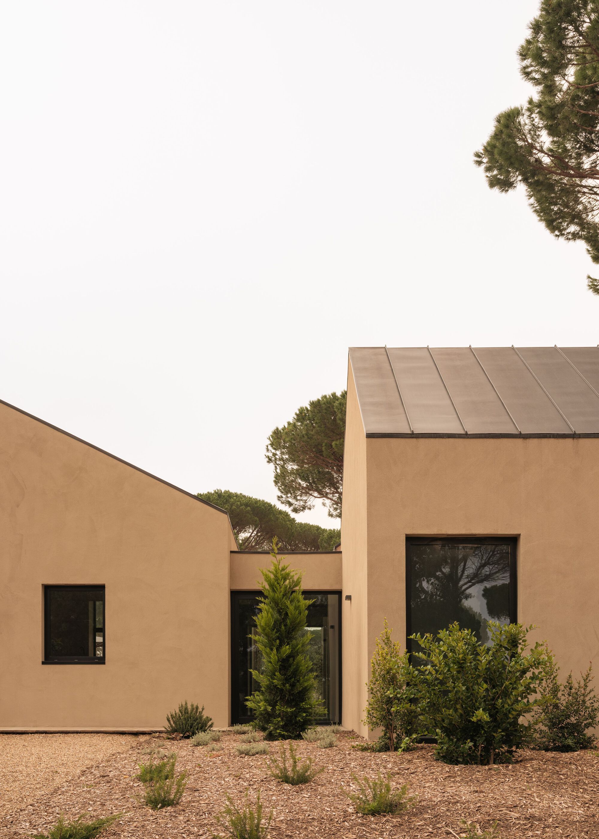 Ochre stucco volumes with metal roofs and planted courtyard with gravel and shrubs