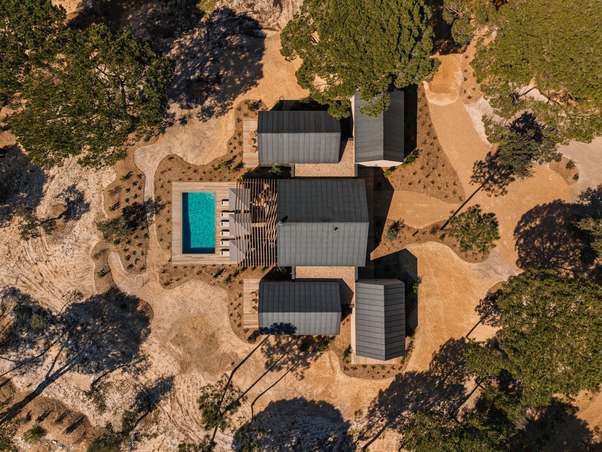 Aerial view of dark metal roofs clustered around a pool in sandy landscape with trees